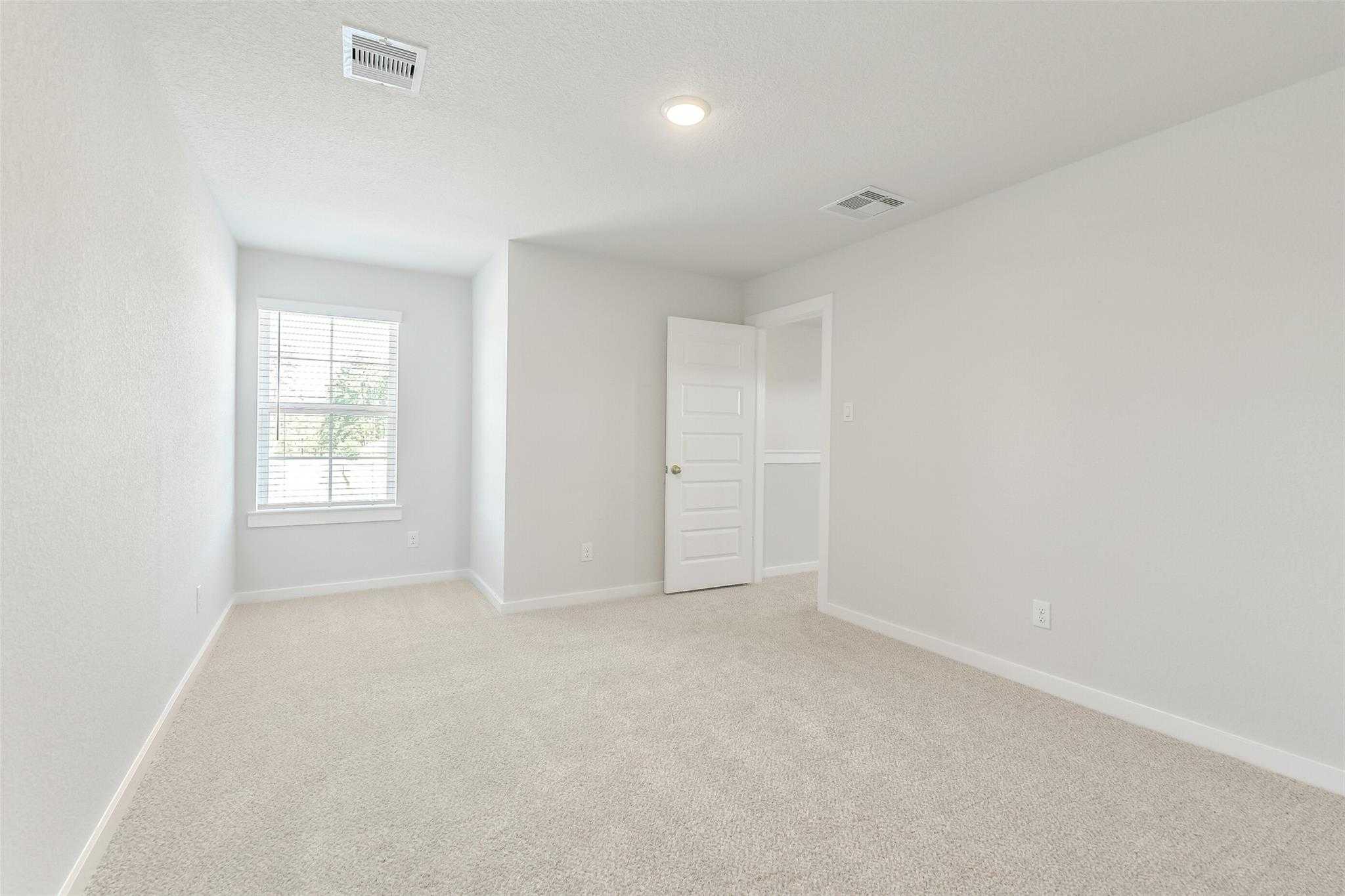 Bright secondary bedroom with large window, neutral walls, and carpeted floor in The San Marcos E home, Cleveland, Texas