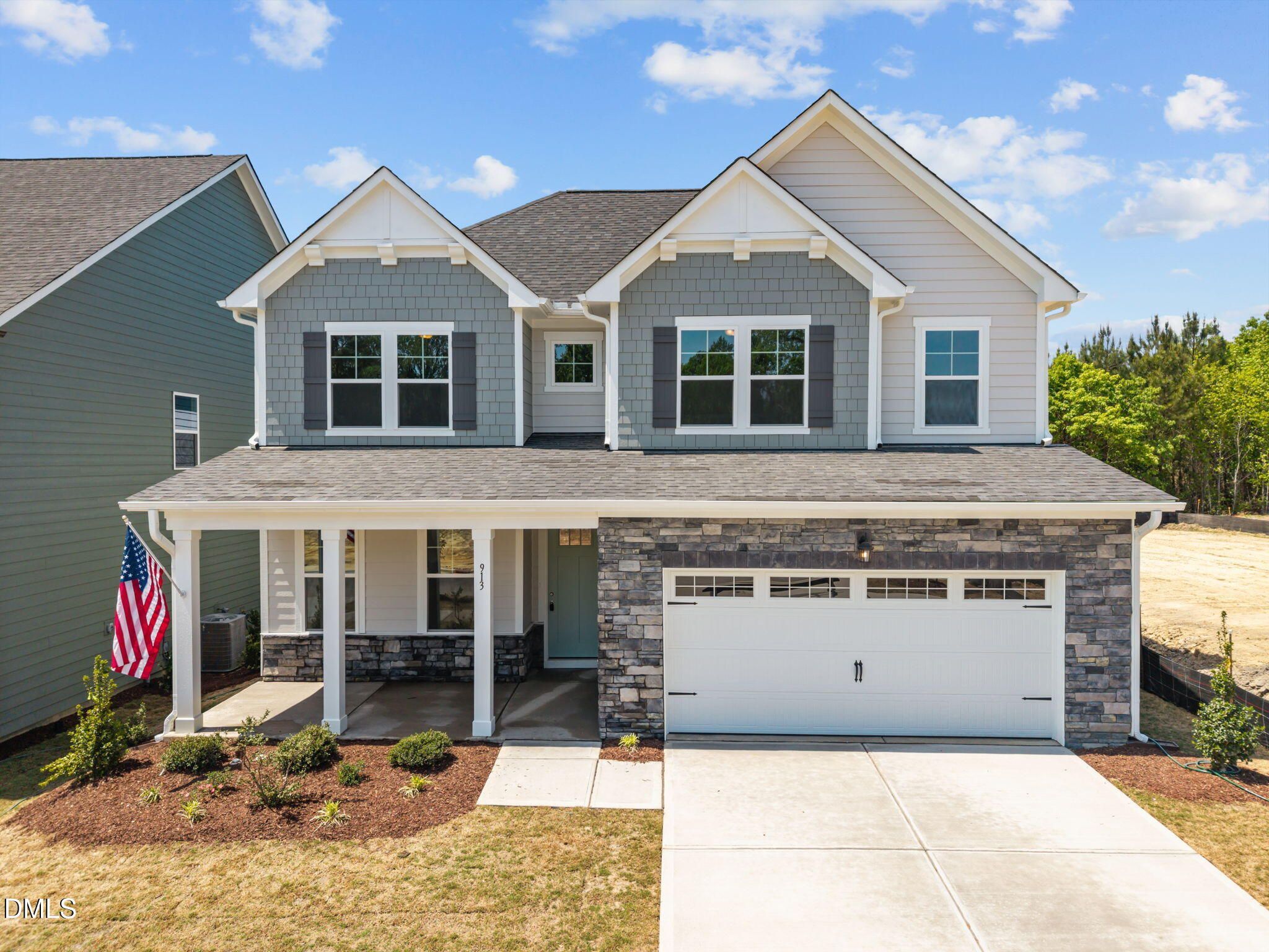 Modern two-story gray and white home with covered porch, American flag, stone garage, and driveway in Wendell Ridge, NC