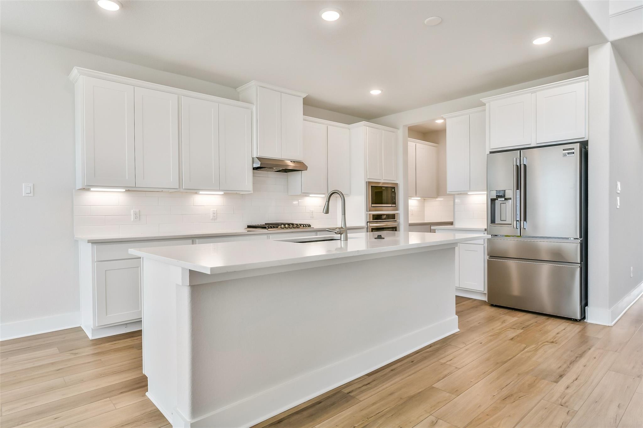 Modern white kitchen with quartz island, stainless steel fridge, gas range, subway tile backsplash in Davidson Homes Victoria A, Texas City