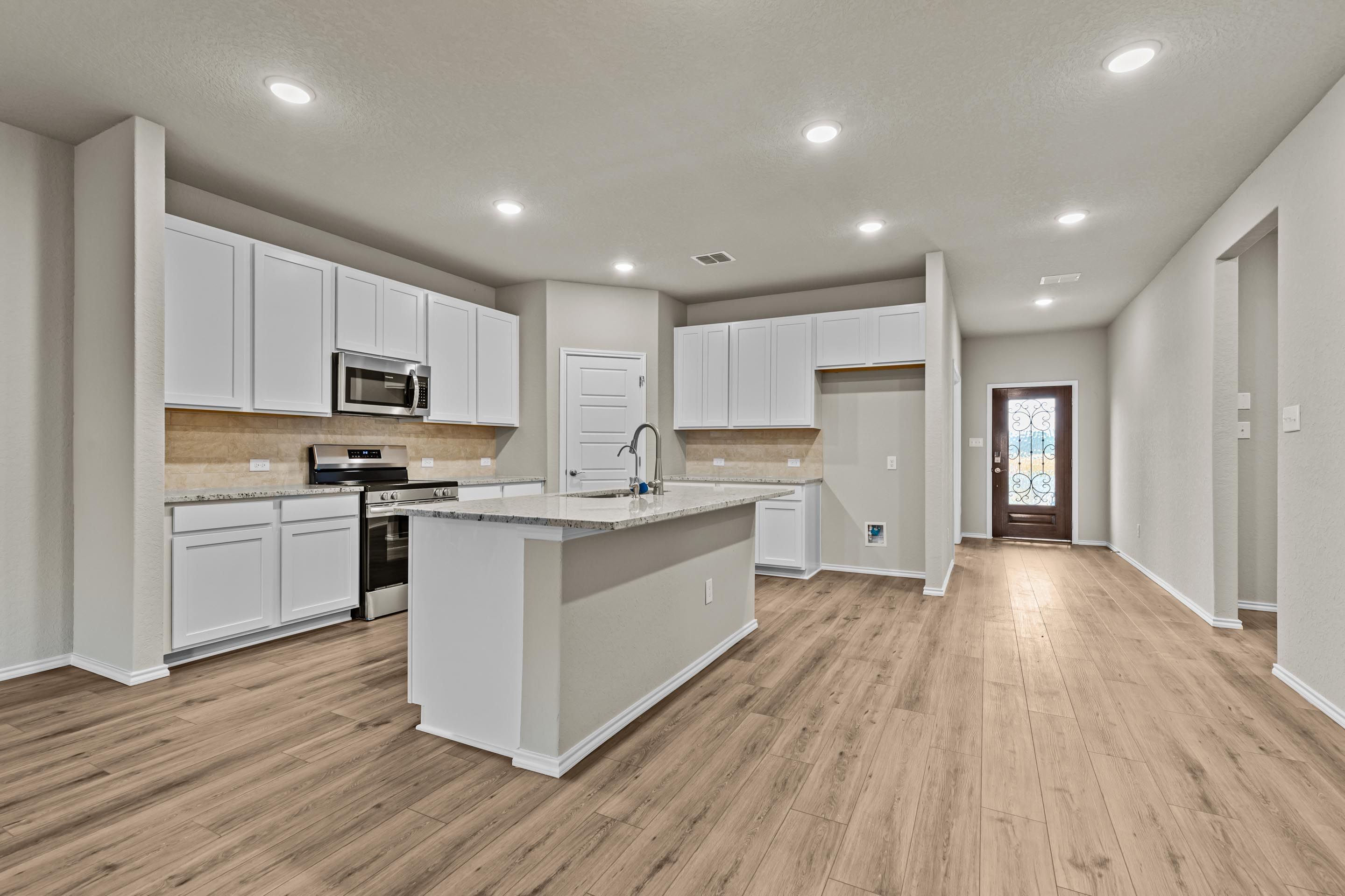 Modern white kitchen with large island, stainless appliances, quartz counters, wood floors in Davidson Homes The Douglas F, San Antonio