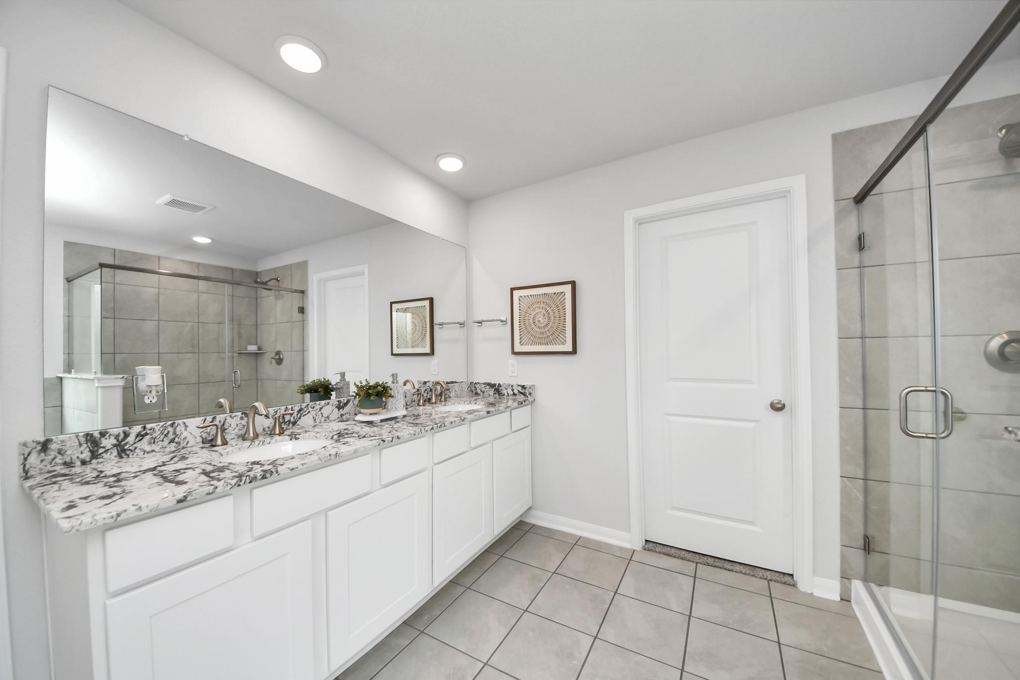 Modern primary bathroom at Sunterra in Katy, TX by Davidson Homes featuring dual vanity and glass-enclosed shower.