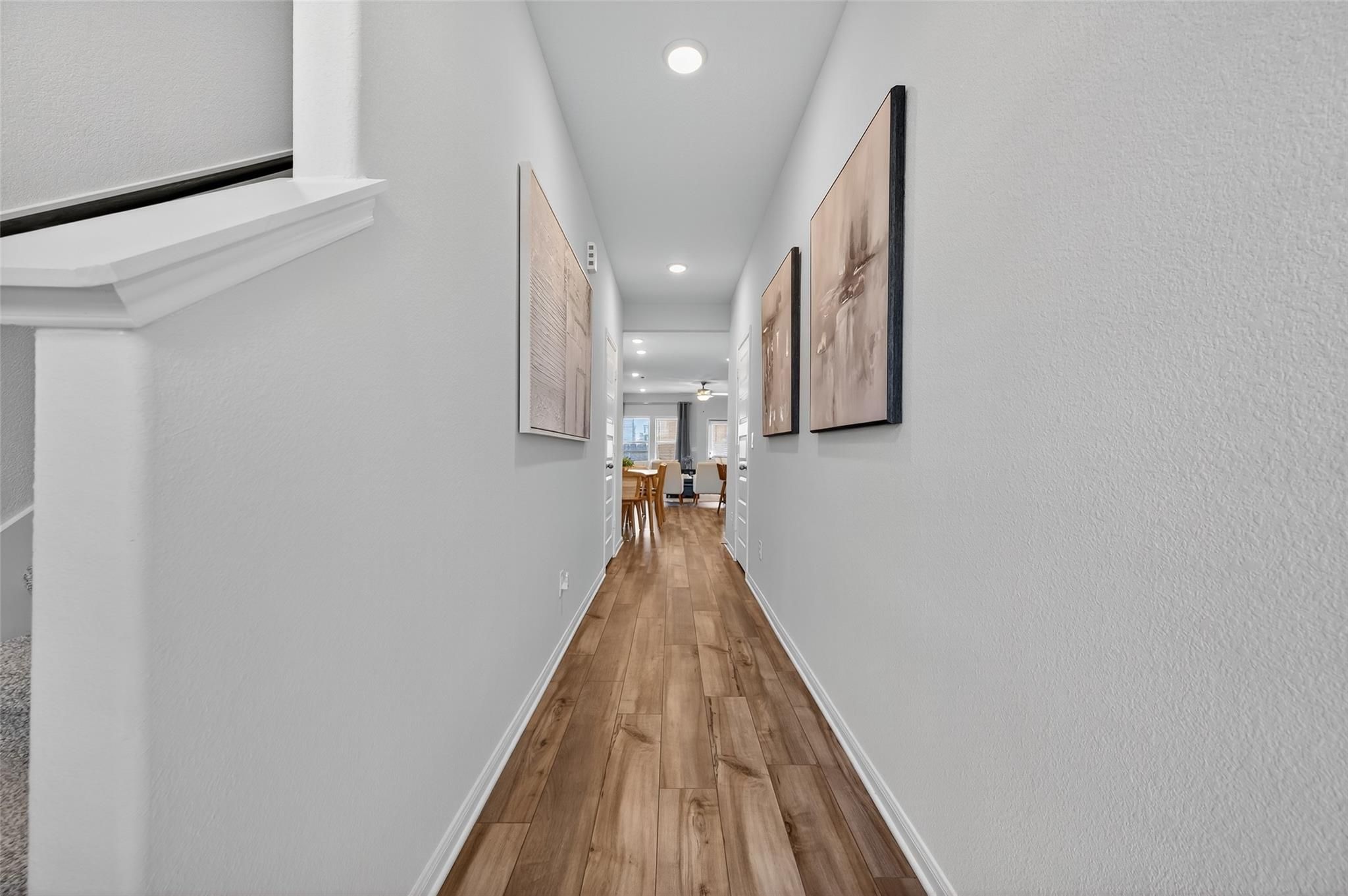 Elegant hallway with light wood floors, white walls, and framed art opening to dining area in Davidson Homes The Brazos E, Magnolia, Texas