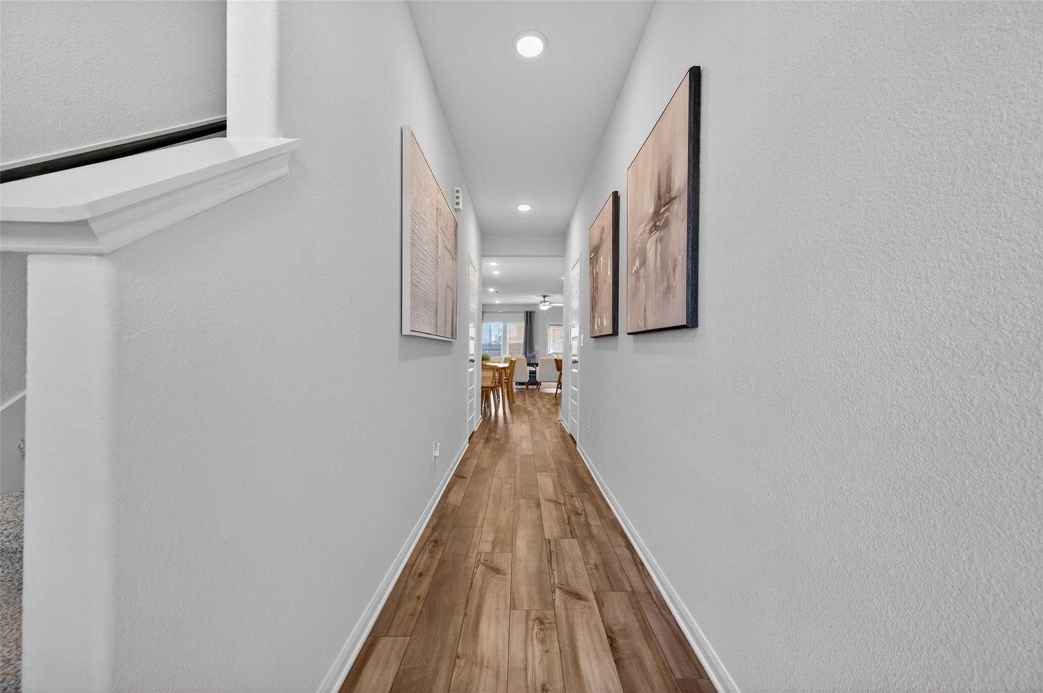 Elegant hallway with light wood floors, white walls, and framed art opening to dining area in Davidson Homes The Brazos E, Magnolia, Texas