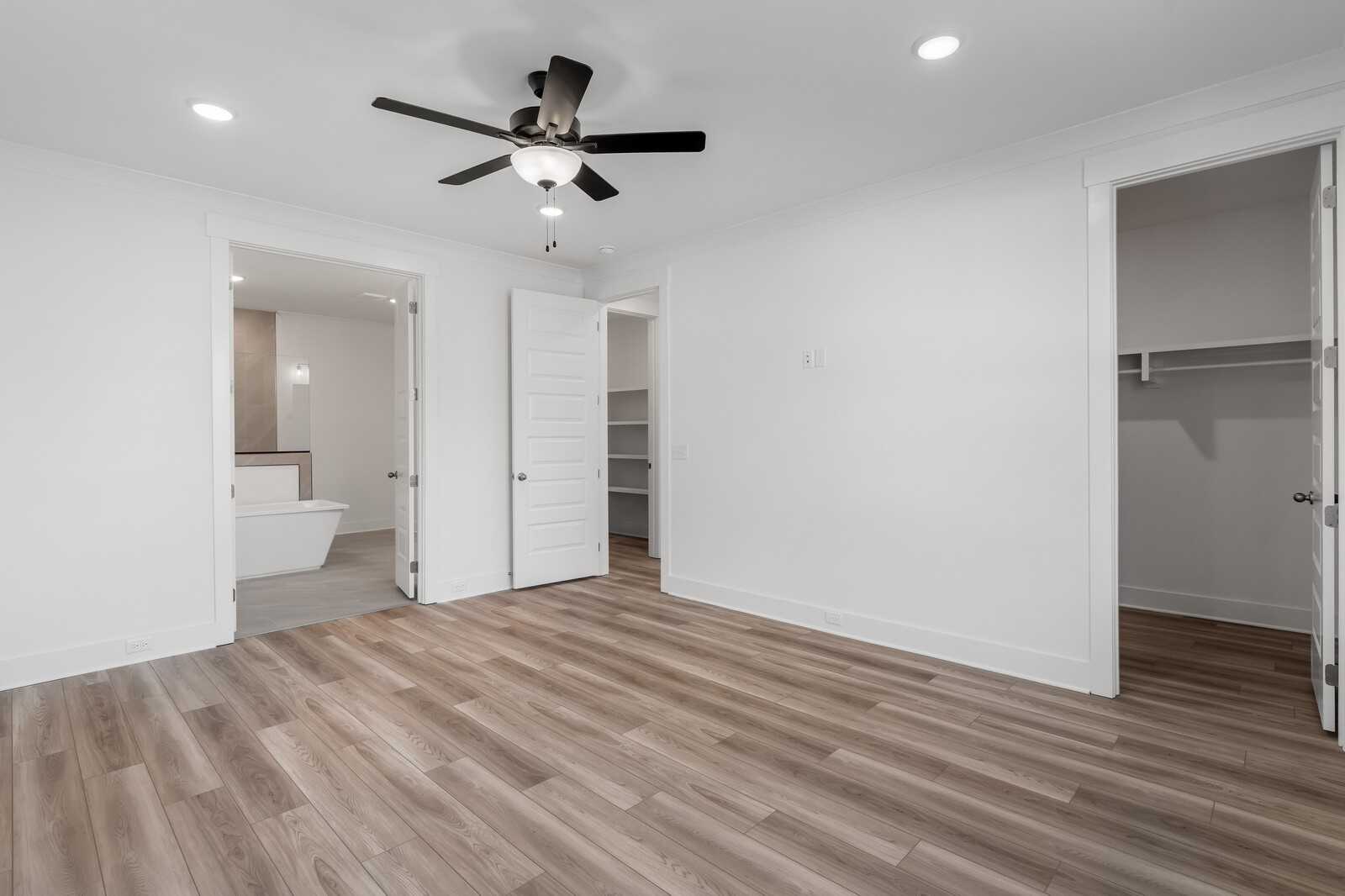 Bright bedroom with ceiling fan, open doors to en-suite bathroom and walk-in closet, hardwood floors in Davidson Homes The Hathaway, Murfreesboro