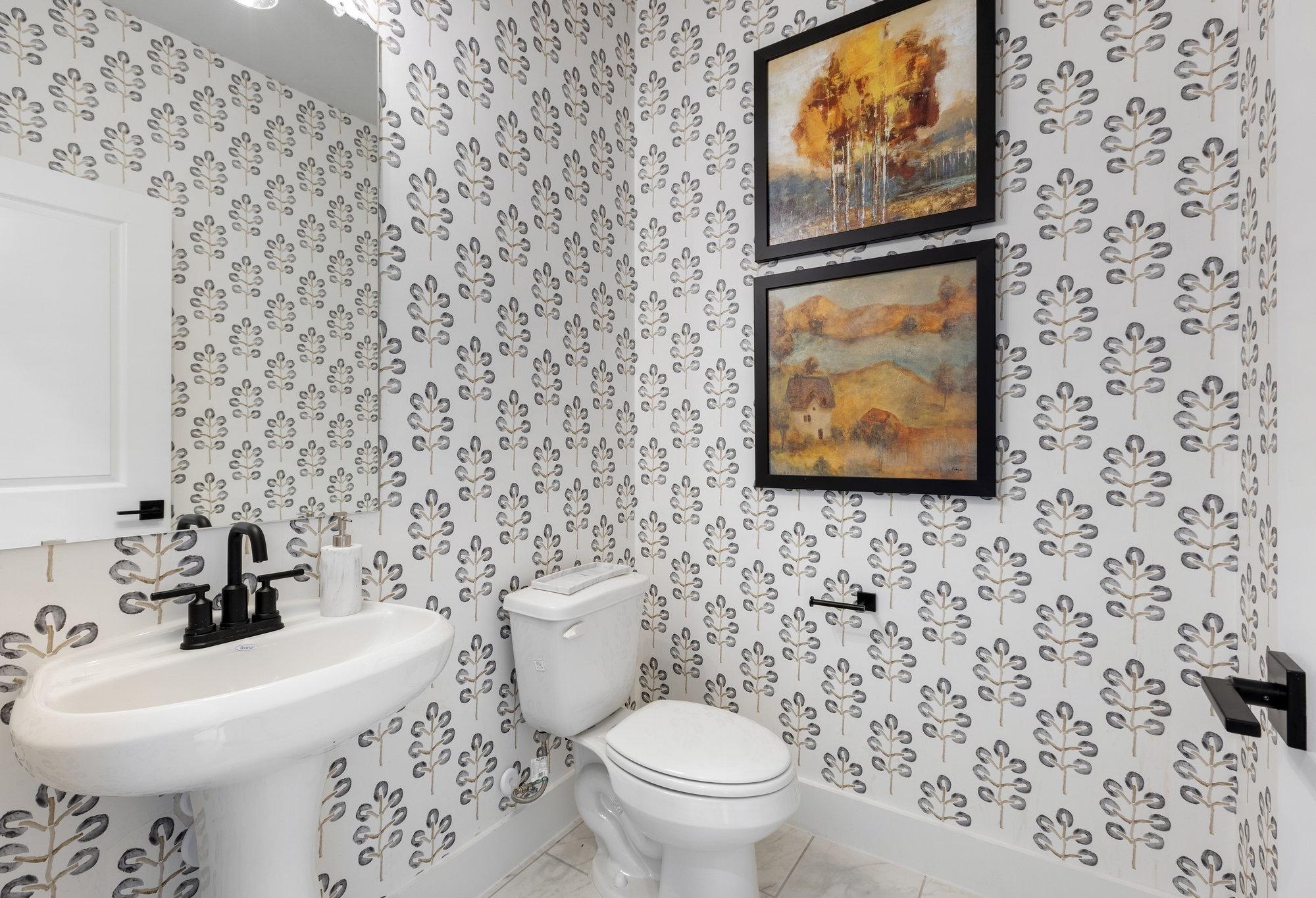 Stylish powder room in The Sequoia with leaf-patterned wallpaper, abstract landscape art, pedestal sink, and toilet