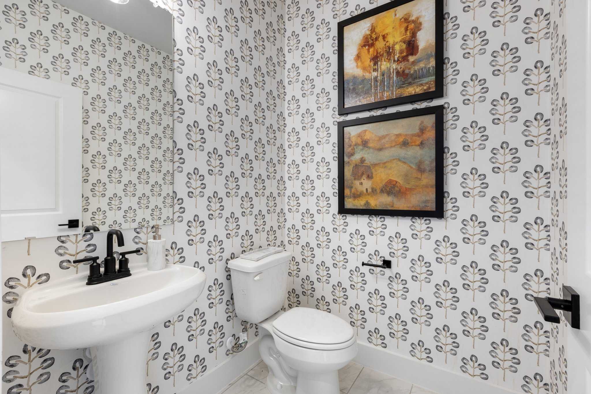 Elegant powder room with leaf-patterned wallpaper, pedestal sink, toilet, and abstract art in Davidson Homes The Sequoia N, Josephine, Texas