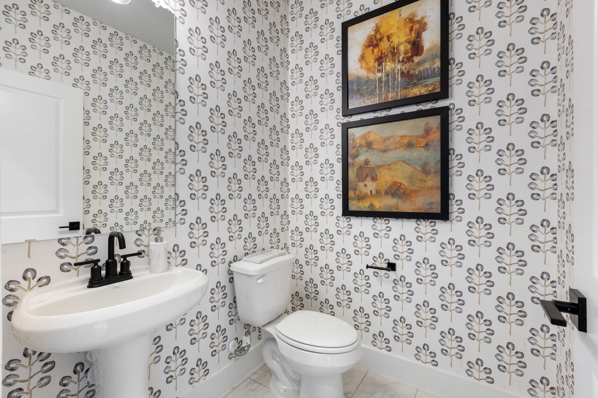 Elegant powder room at Mercer Meadows in Royse City TX with leaf-patterned wallpaper, pedestal sink, and abstract wall art