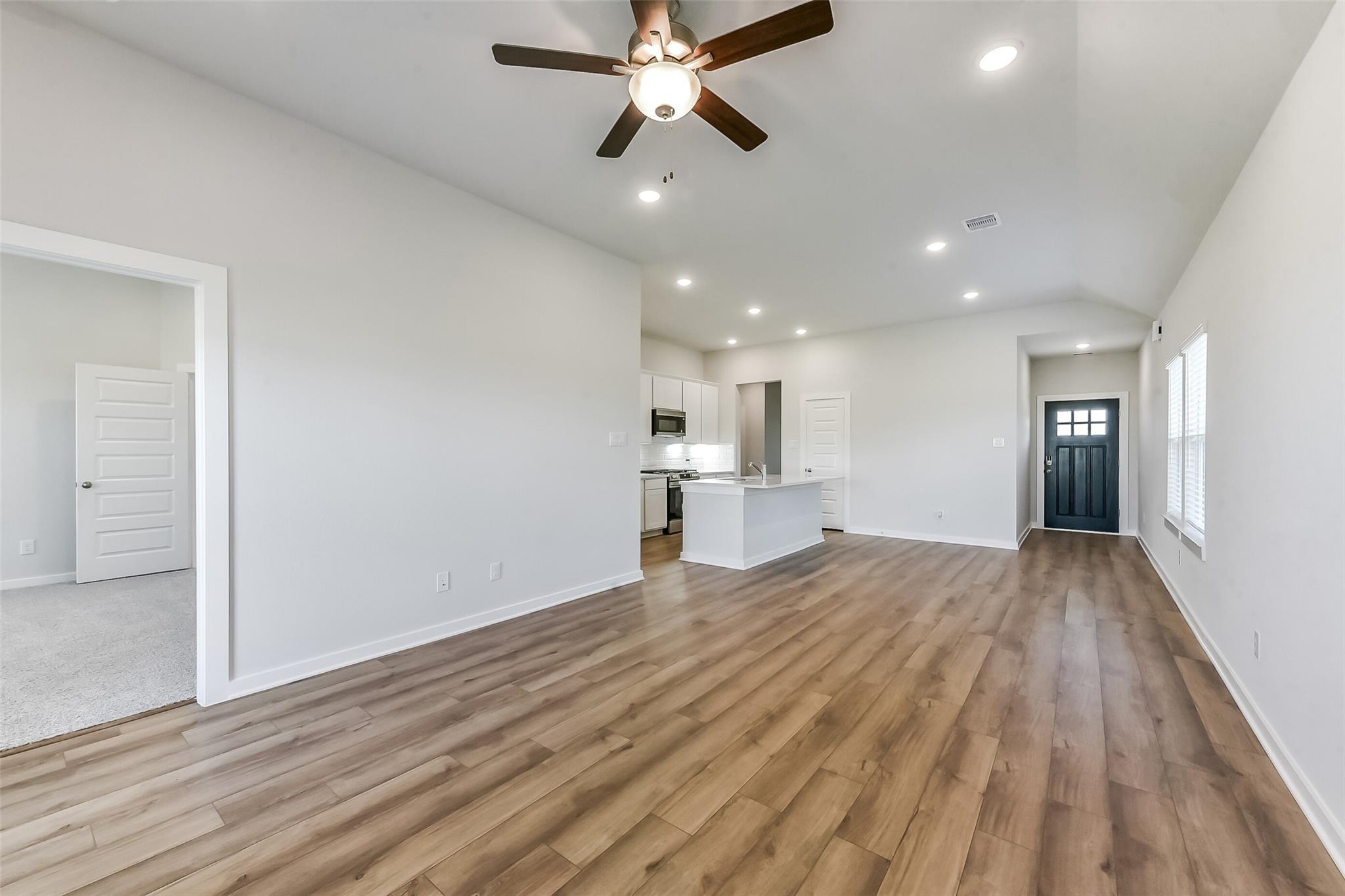 Open-concept living room with kitchen island, white cabinets, hardwood floors, and ceiling fan in Davidson Homes The Costa B, Dayton, Texas
