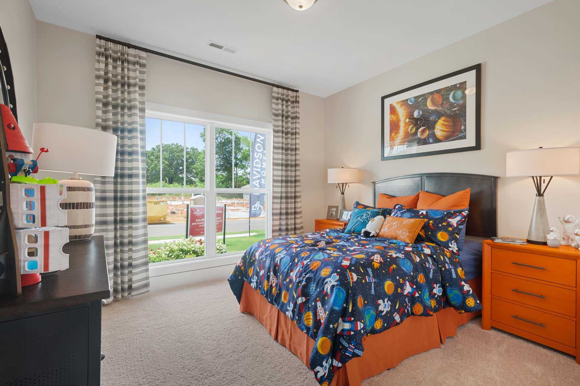 Space-themed child's bedroom at Flint Meadows in New Market Alabama with navy planet bedding, orange accents, and toys