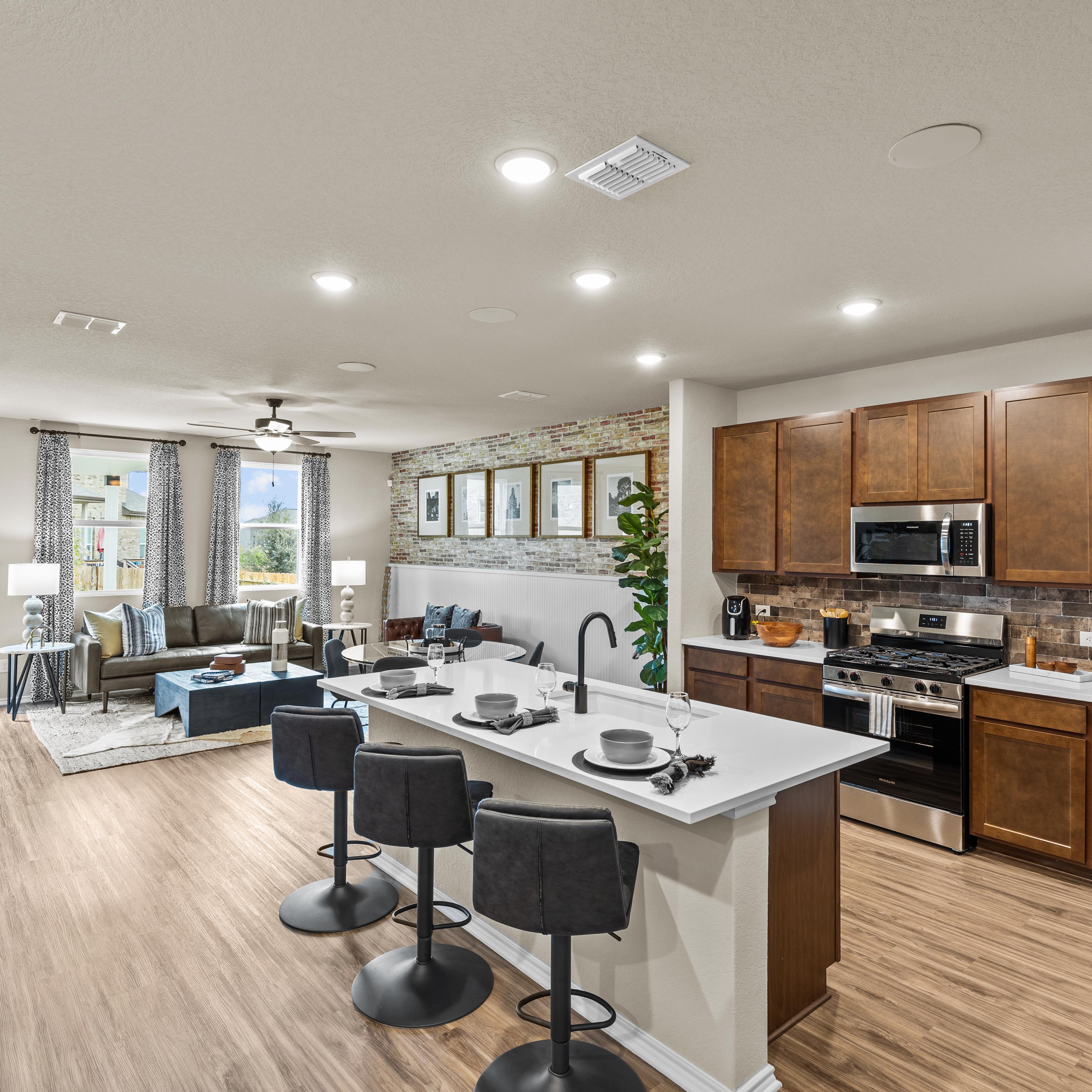 Spacious open-concept kitchen and living room at Bricewood in San Antonio TX with hardwood floors, white island, wood cabinets, and lounge seating