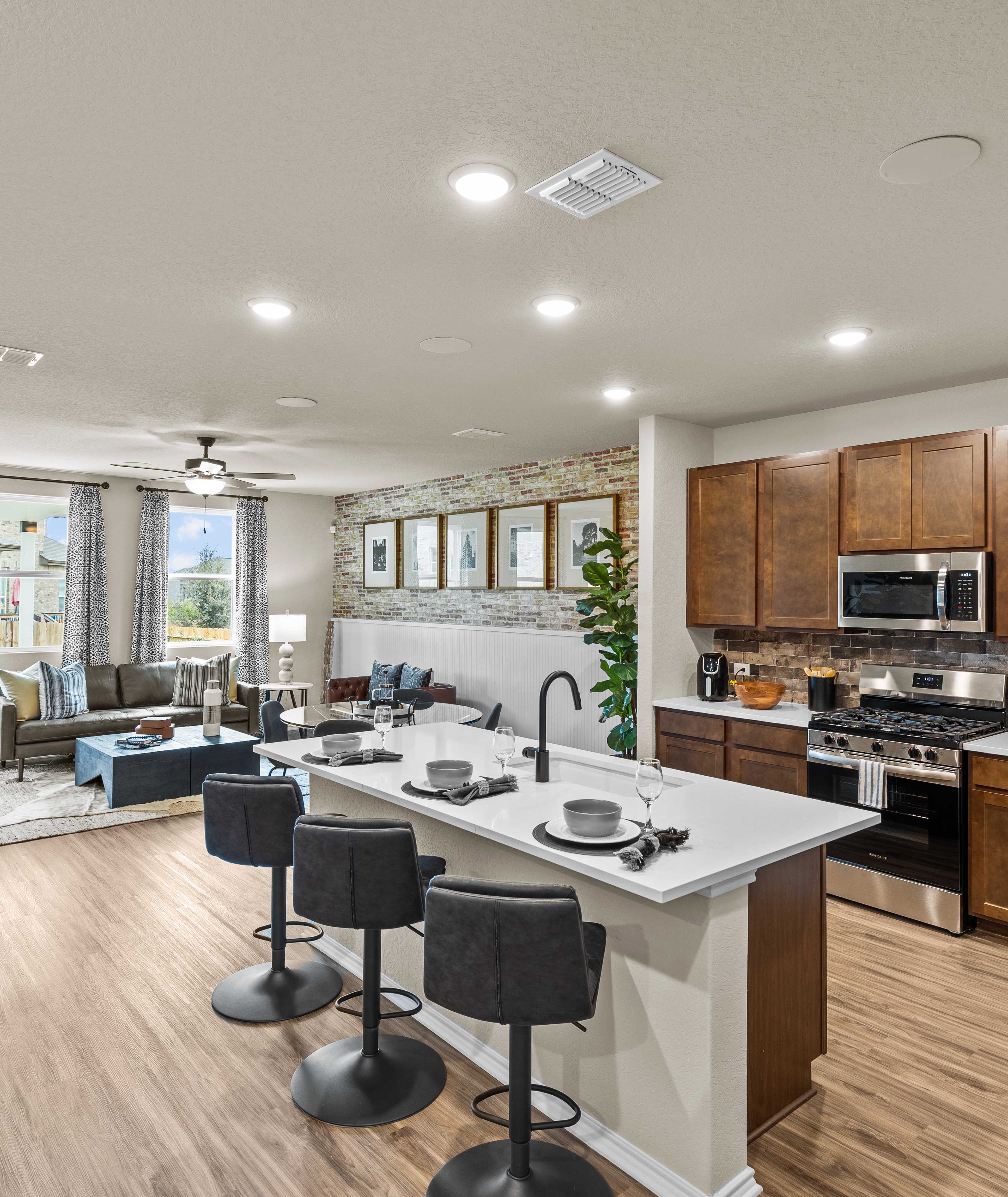 Spacious open-concept kitchen and living room at Bricewood in San Antonio TX with hardwood floors, white island, wood cabinets, and lounge seating