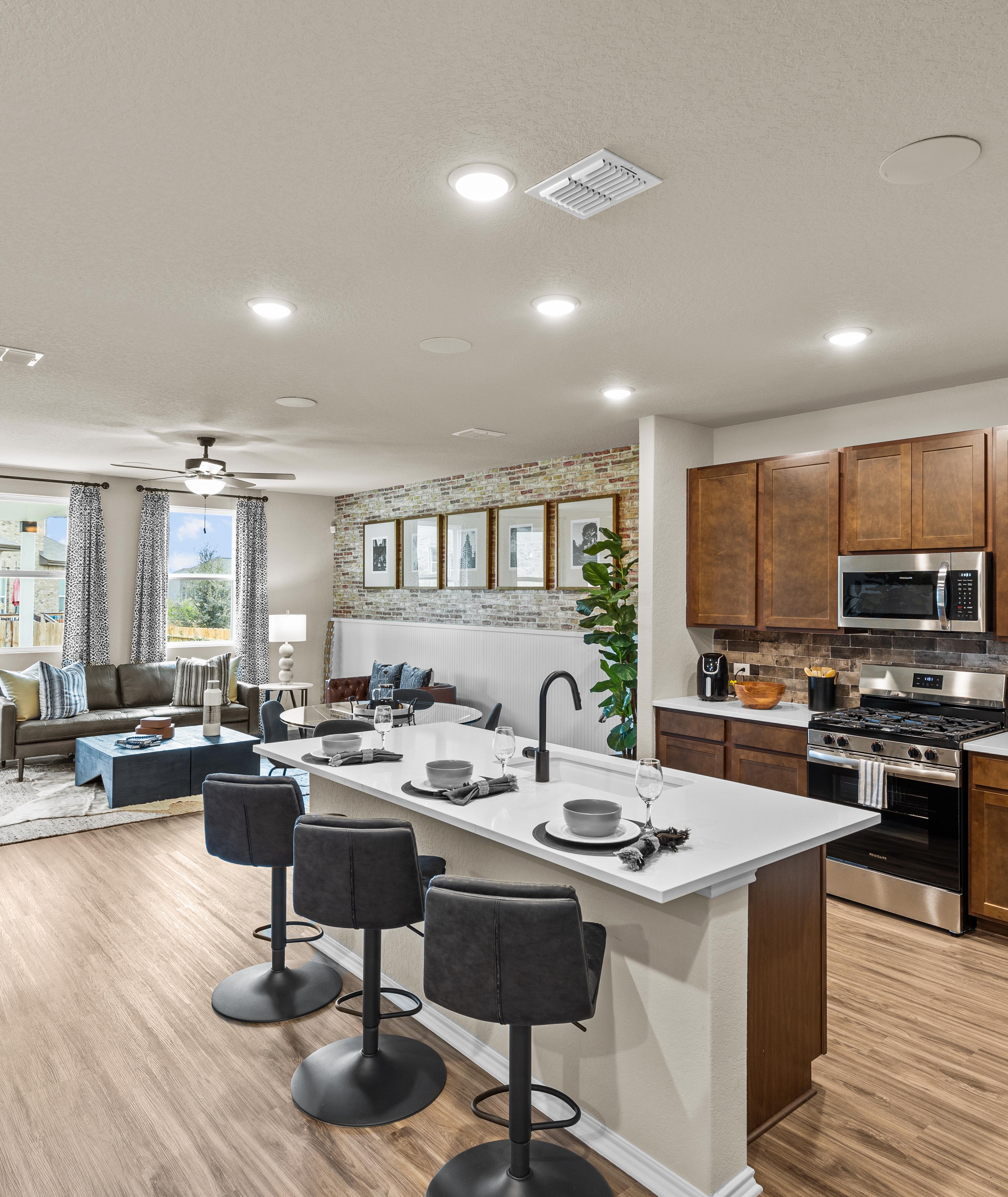 Spacious open-concept kitchen and living room at Bricewood in San Antonio TX with hardwood floors, white island, wood cabinets, and lounge seating