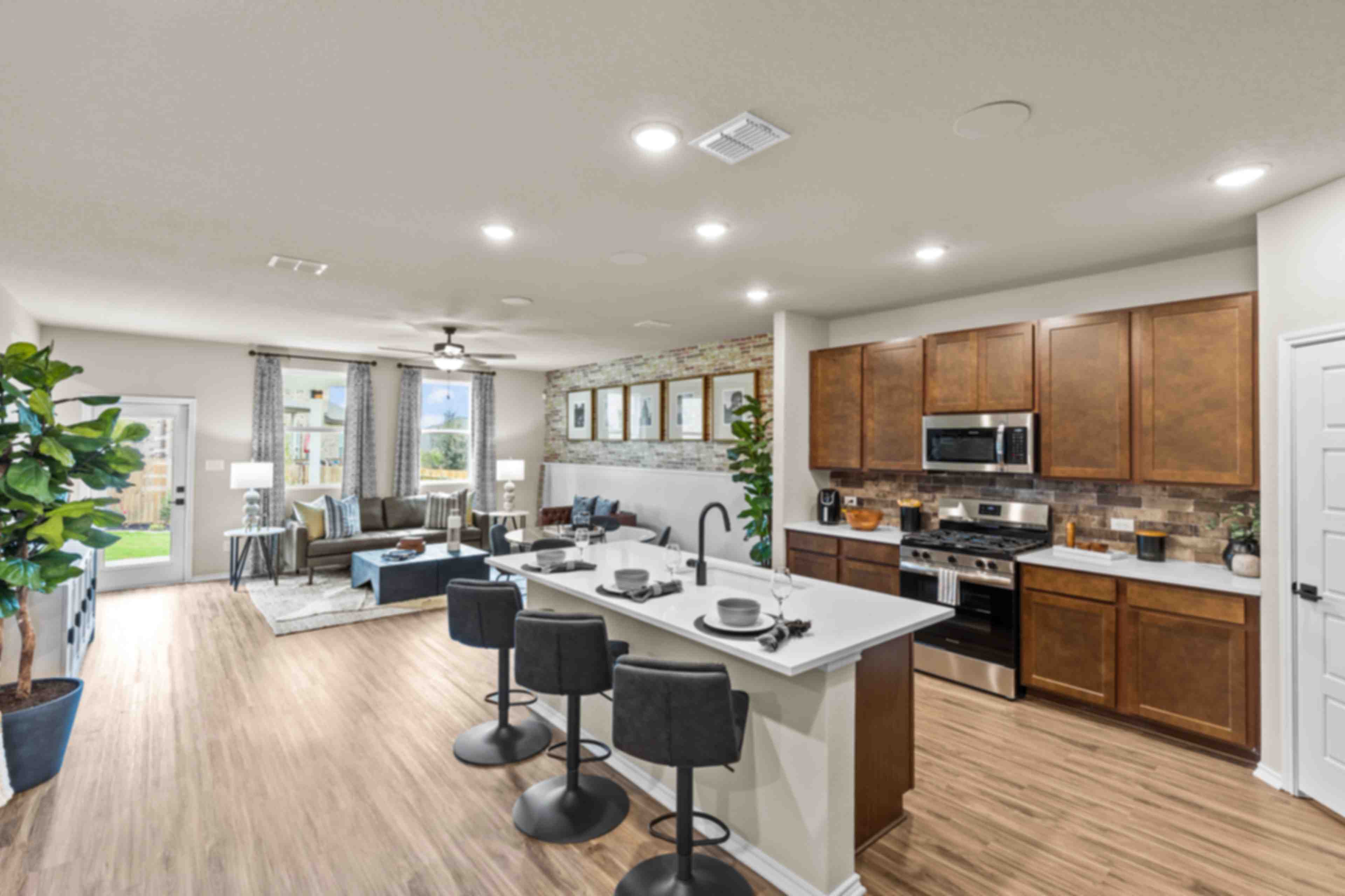 Spacious open-concept kitchen and living room at Bricewood in San Antonio TX with hardwood floors, white island, wood cabinets, and lounge seating