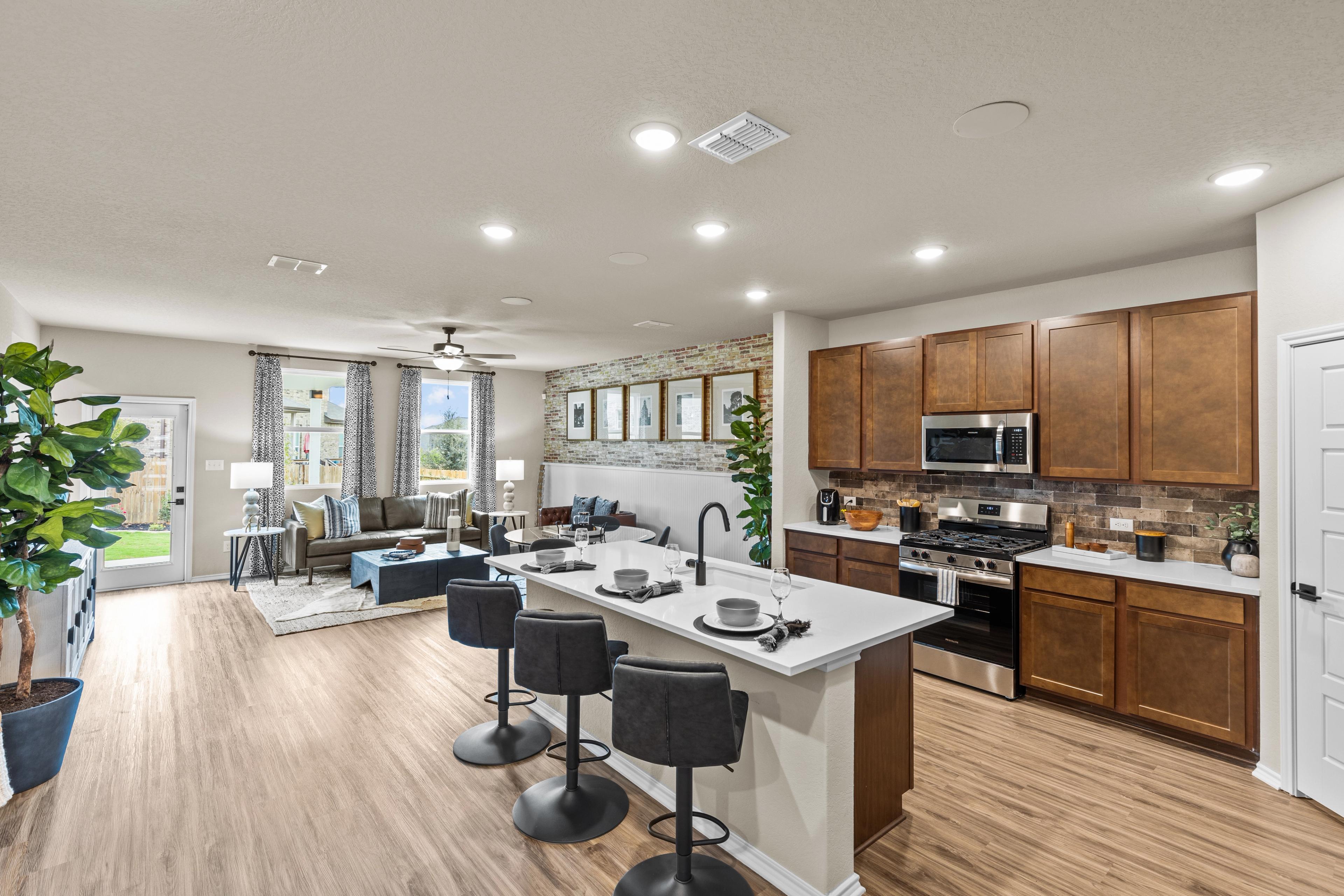 Open-concept kitchen and living room in Morgan Meadows San Antonio TX home by Davidson Homes featuring quartz island, hardwood floors, and brick accent wall