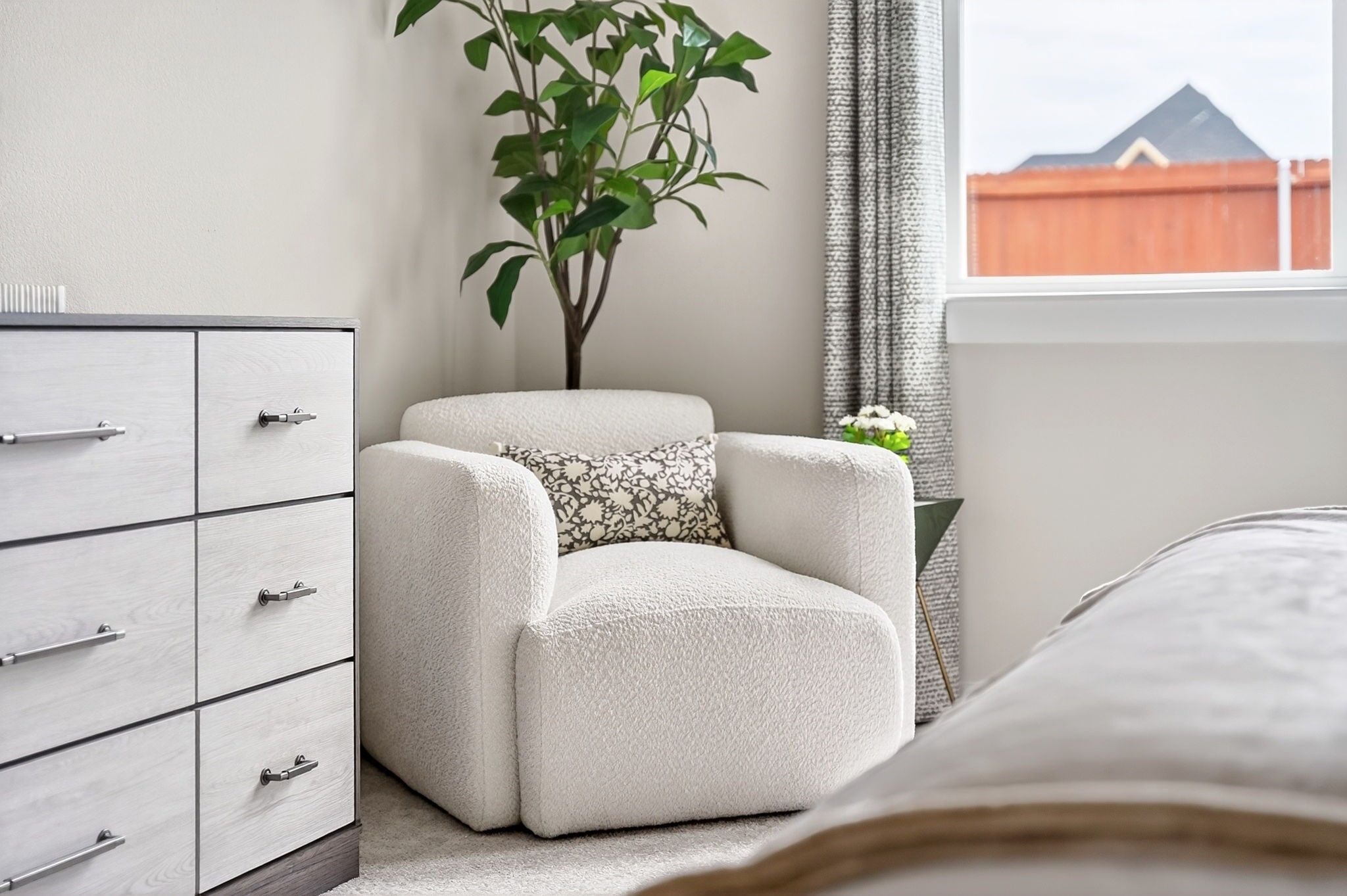Cozy bedroom reading nook with white boucle armchair in The Laurel G floor plan by Davidson Homes in Heartland, Texas.