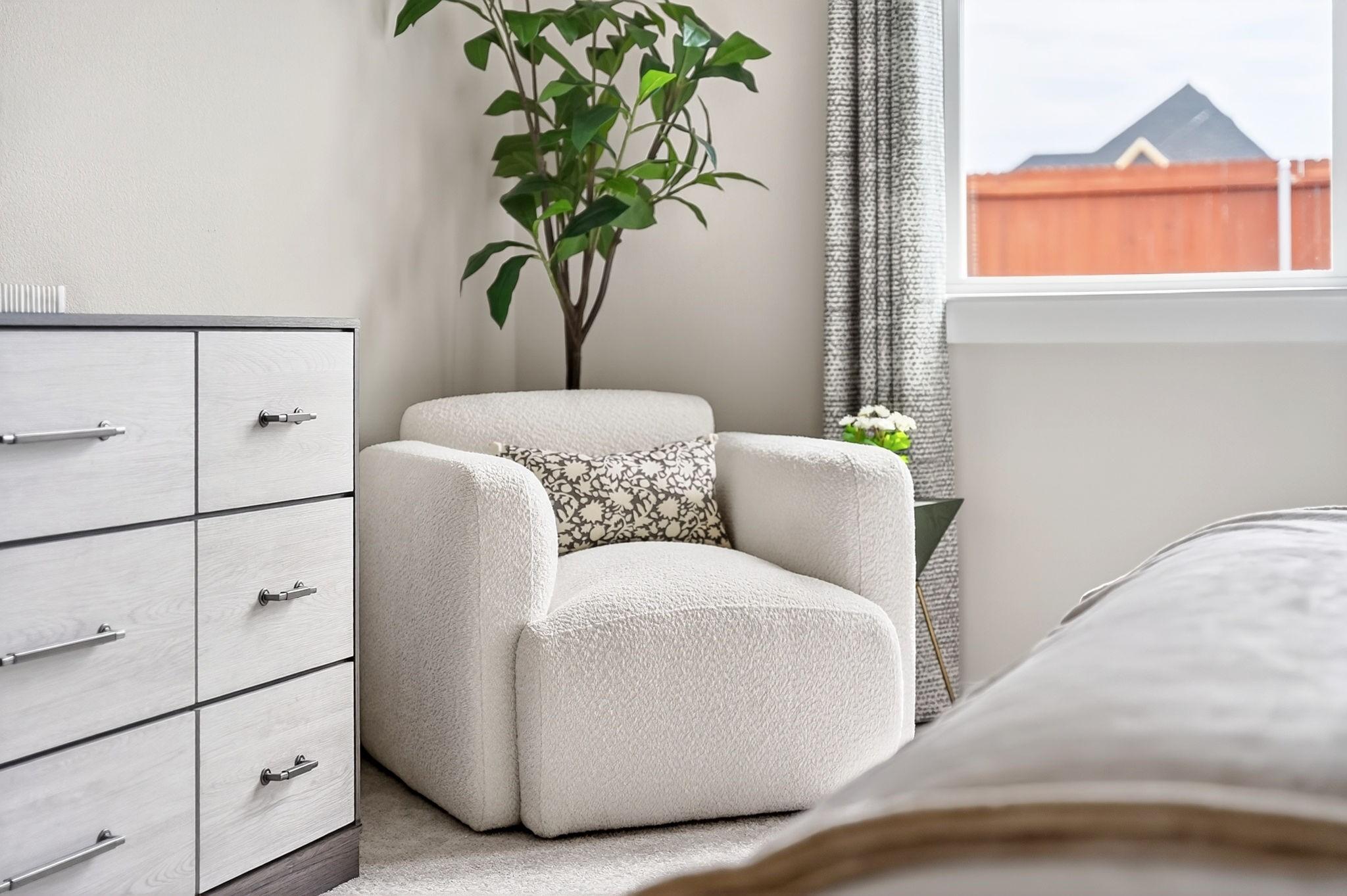 Cozy bedroom reading nook with white boucle armchair in The Laurel G floor plan by Davidson Homes in Heartland, Texas.