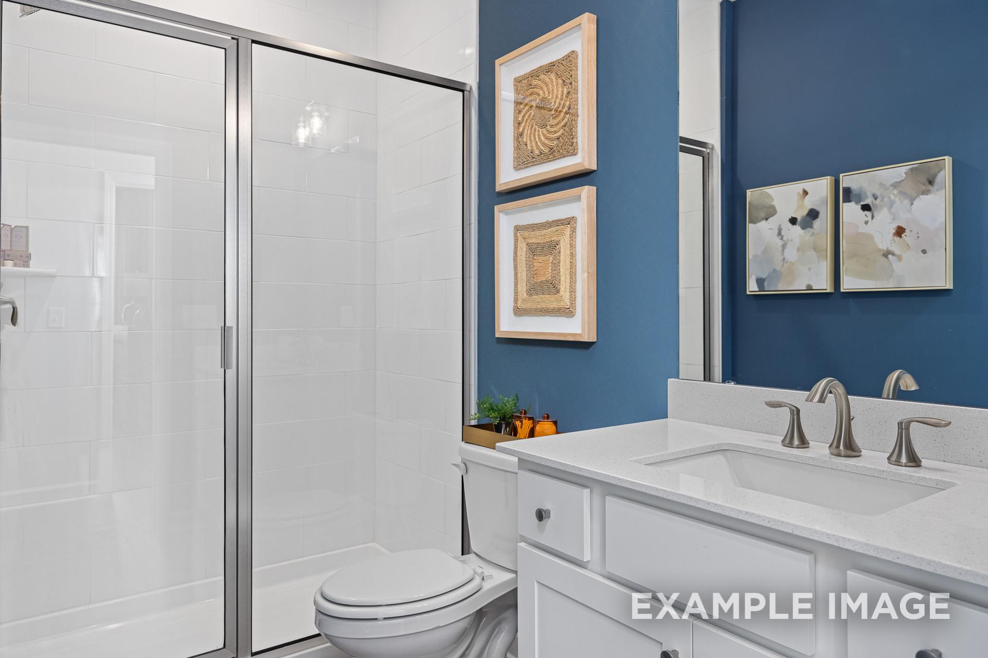 Modern master bathroom in The Adalynn C featuring frameless glass shower, white vanity with sink, blue accent wall, and abstract art
