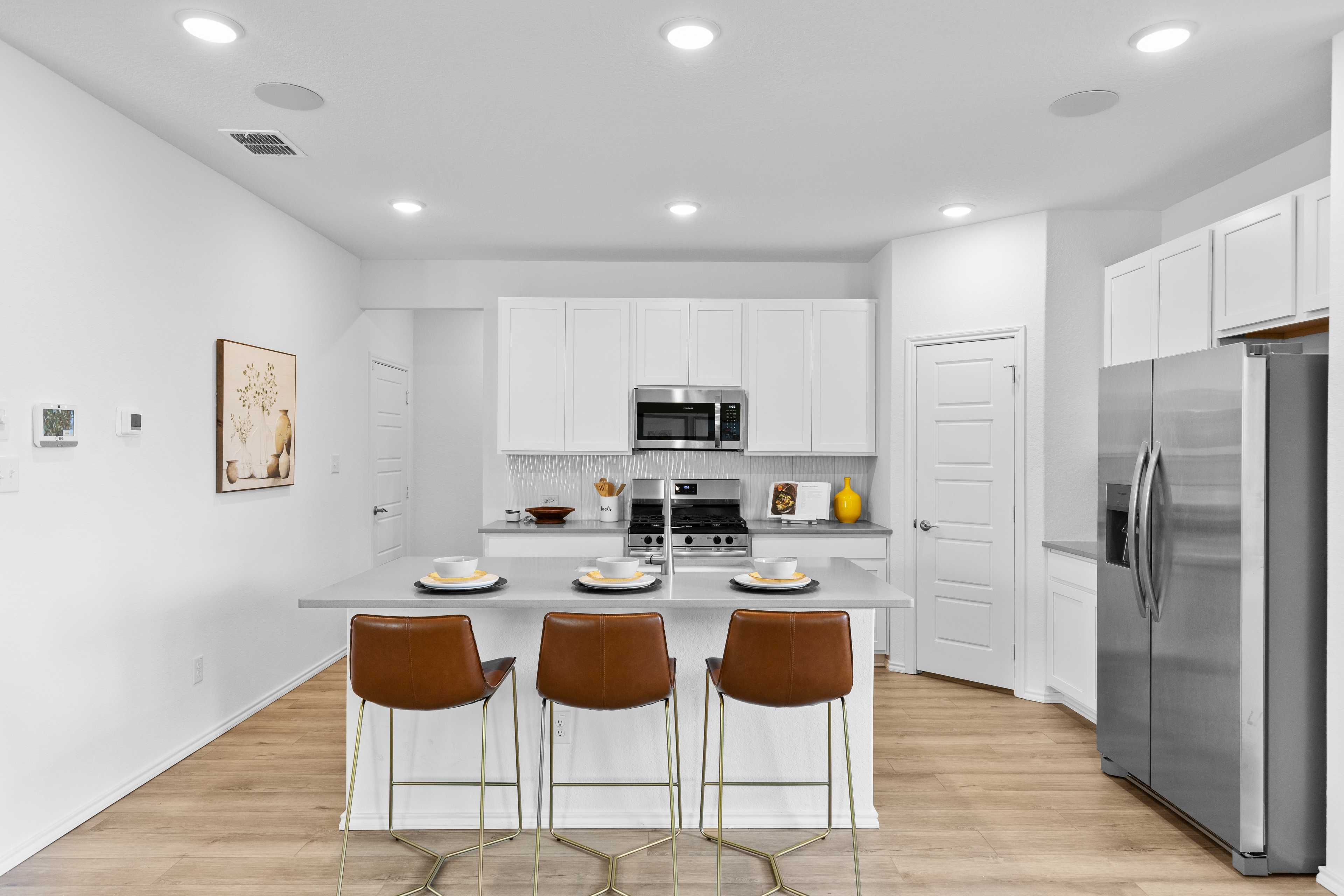 Modern white kitchen at Horizon Pointe in Converse Texas with large island brown leather stools stainless appliances