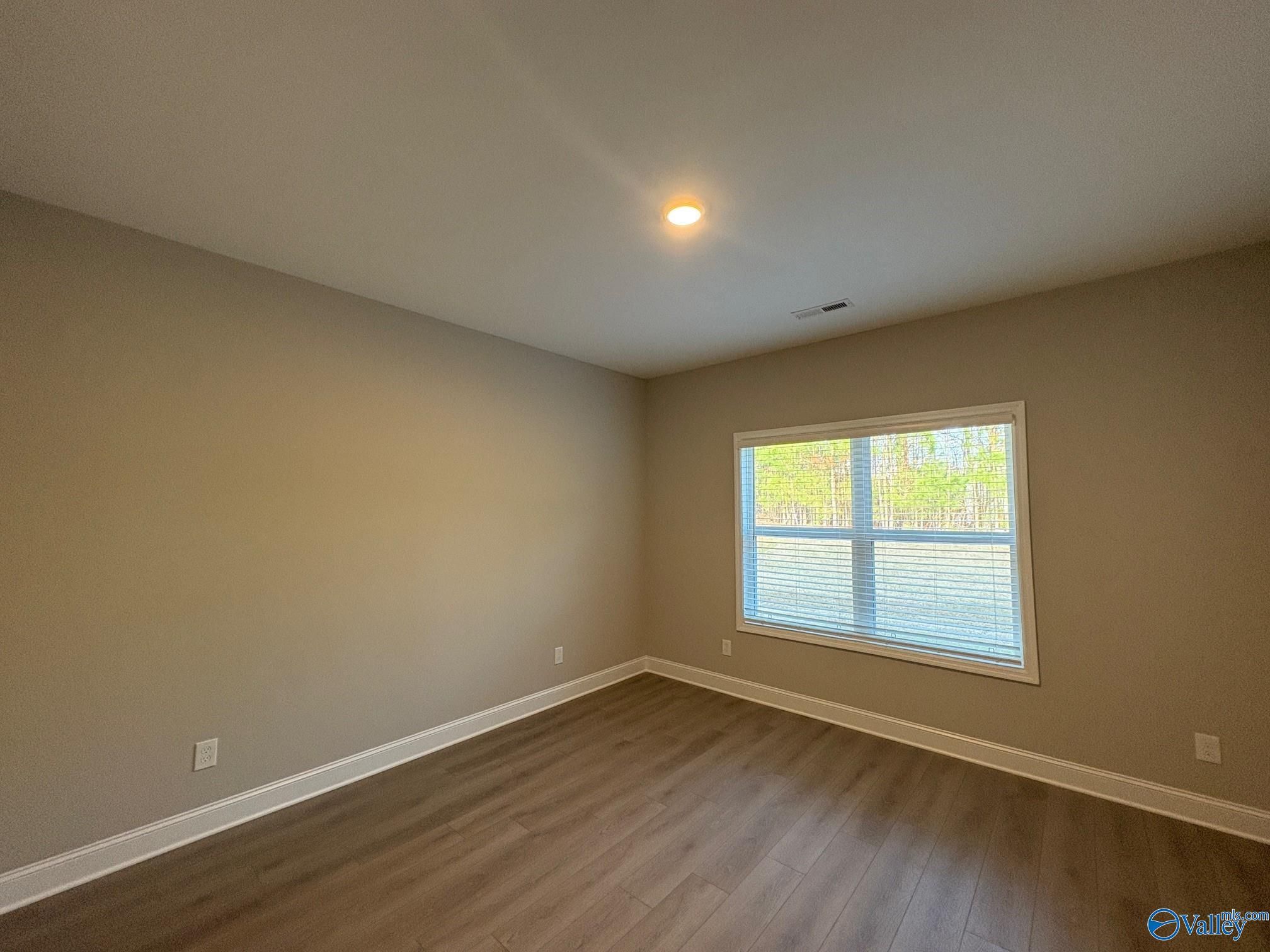 Spacious empty bedroom with large window, beige walls, and hardwood floors in Davidson Homes The Asheville C, Arab Alabama