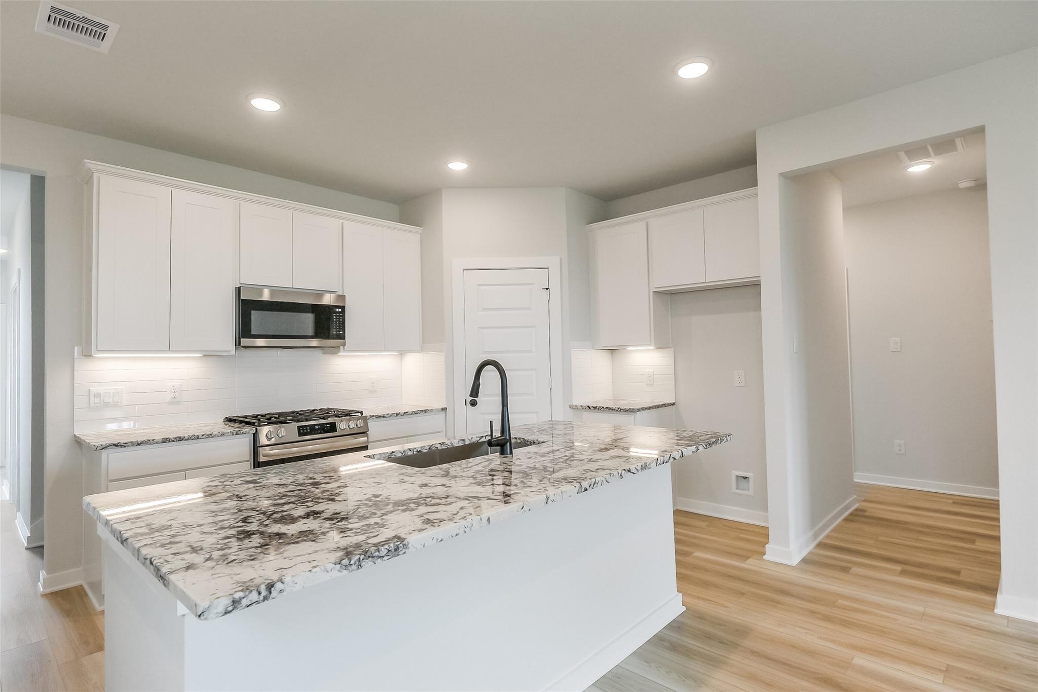 Modern white kitchen with quartz island, stainless appliances, and open layout in Davidson Homes The San Marcos E, Beasley, TX
