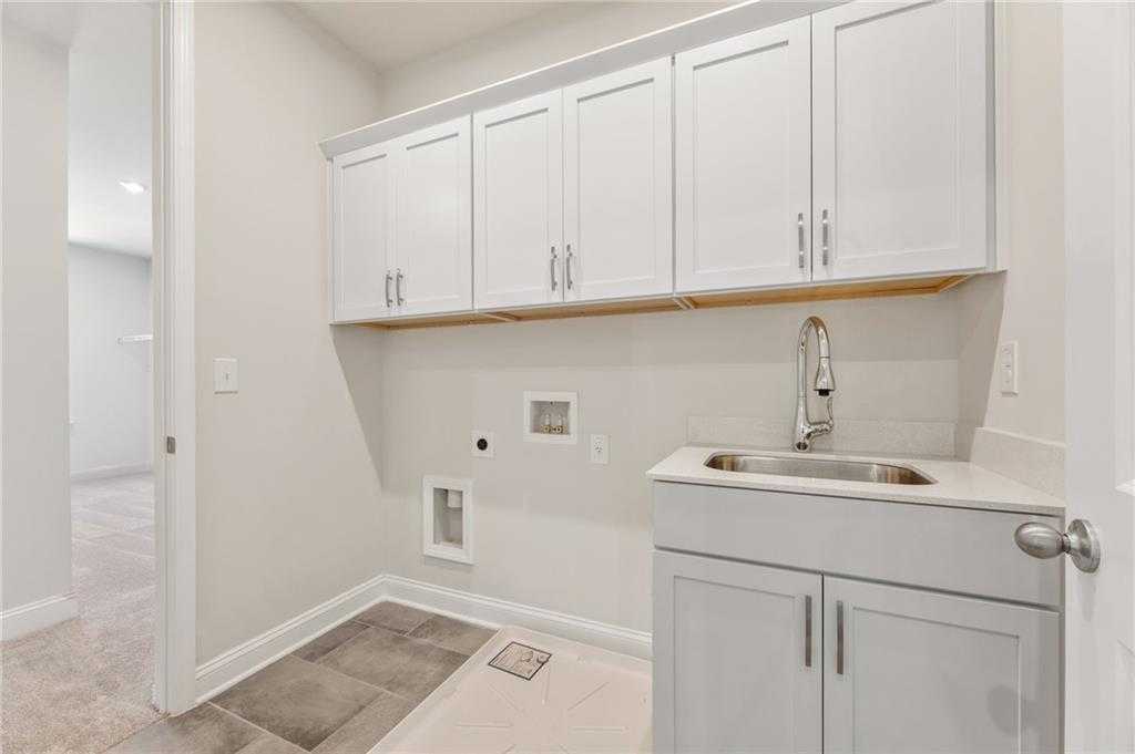 Modern laundry room with white shaker cabinets, gray vanity, stainless sink, and washer/dryer hookups in The Danbury E, Buford, Georgia