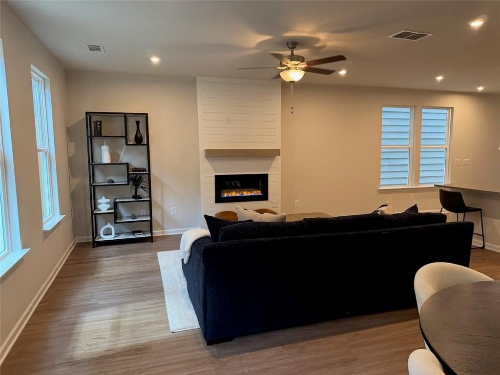 Cozy living room with gas fireplace, black L-shaped sofa, bookshelf, and hardwood floors in Davidson Homes The Cary A, Kennesaw, Georgia