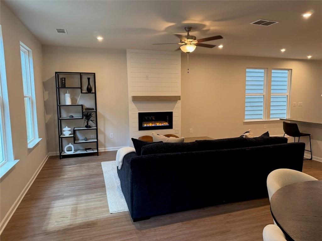 Cozy living room with black sofa, white brick gas fireplace, hardwood floors, and ceiling fan in Davidson Homes The Cary A, Kennesaw, Georgia