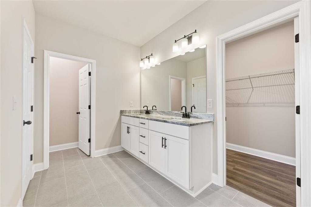 Modern master bathroom featuring double vanity with quartz counters, mirrors, and open walk-in closet in Davidson Homes The Harrison G, Hoschton, GA
