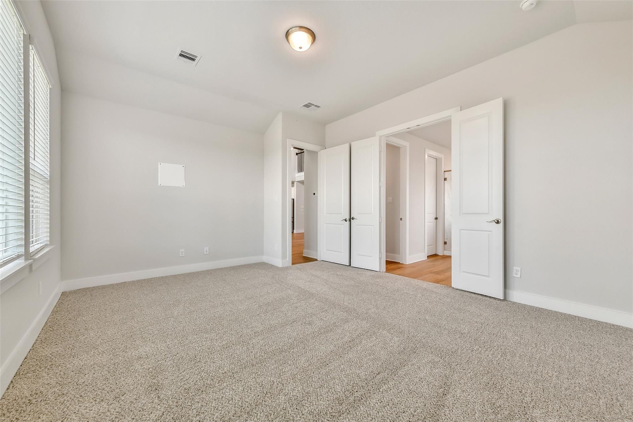 Spacious empty bedroom with beige carpet, open white doors, and natural light in Davidson Homes The Victoria A, Lago Mar, Texas City