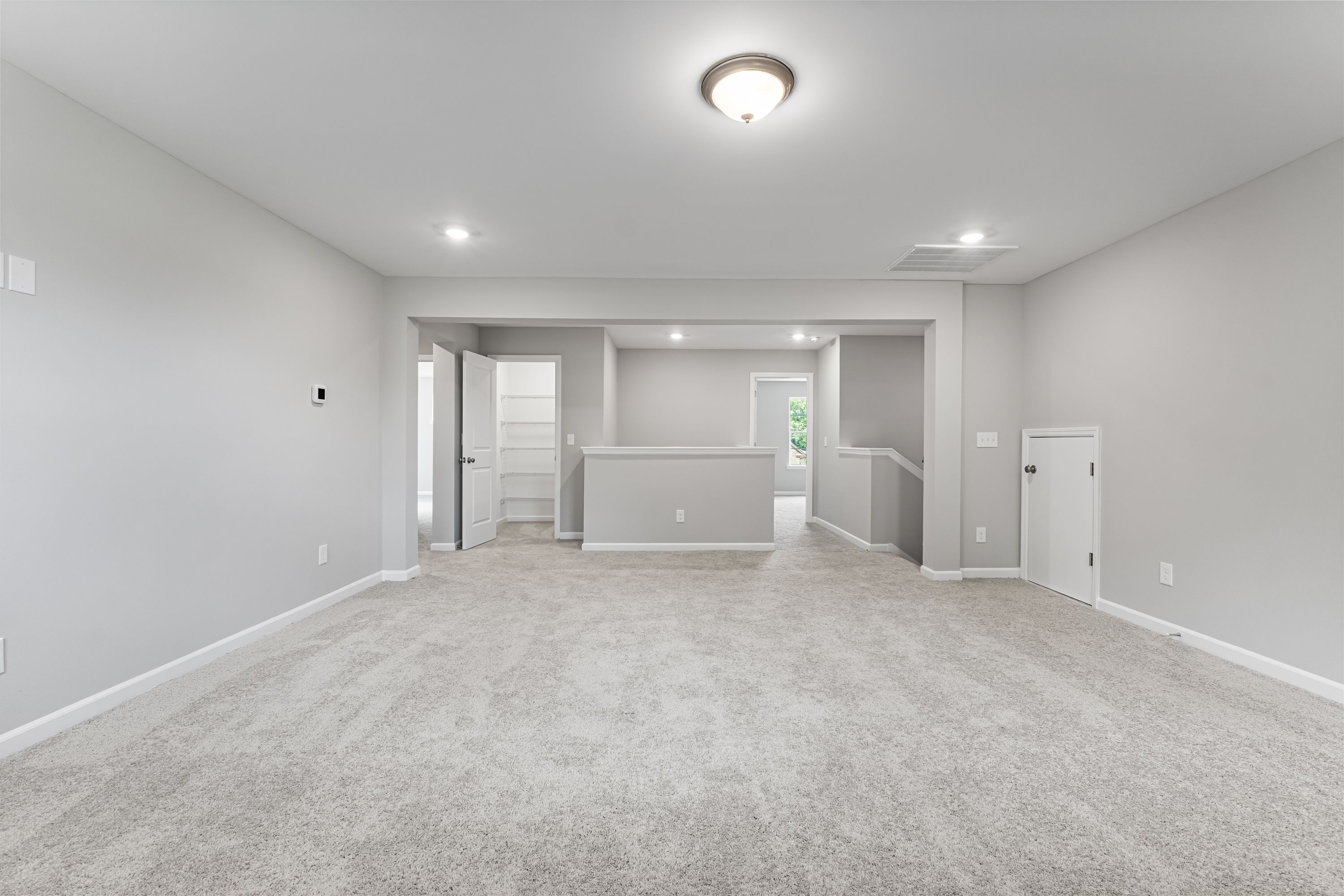 Spacious main floor living area in The Avalon E with light gray walls, beige carpet, recessed lights, and open staircase