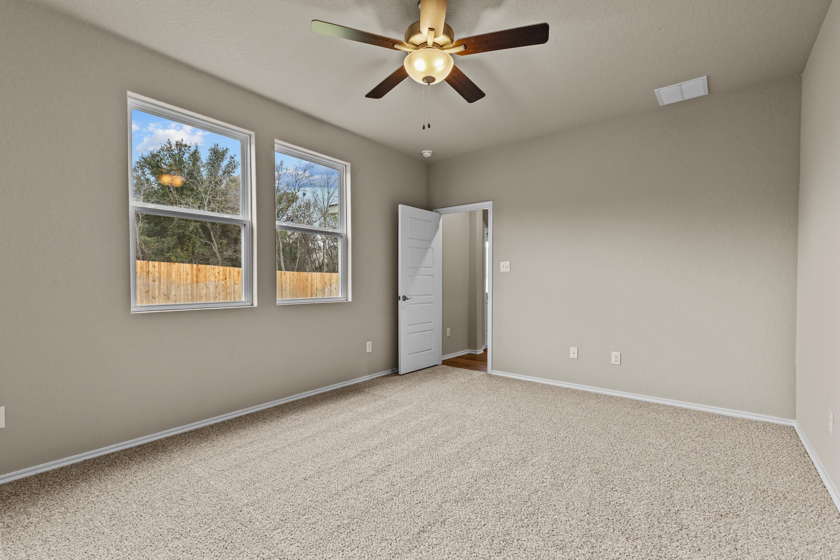 Spacious bedroom with beige carpet, ceiling fan, large windows overlooking fenced yard in Davidson Homes The Douglas F, San Antonio