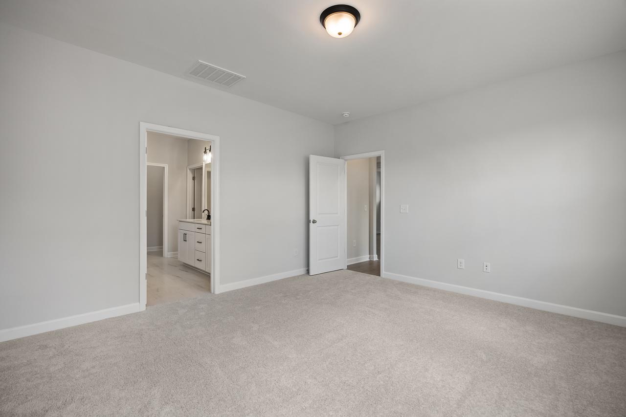 Spacious master suite on the main floor of The Birch II featuring plush carpeting and an attached private bathroom.