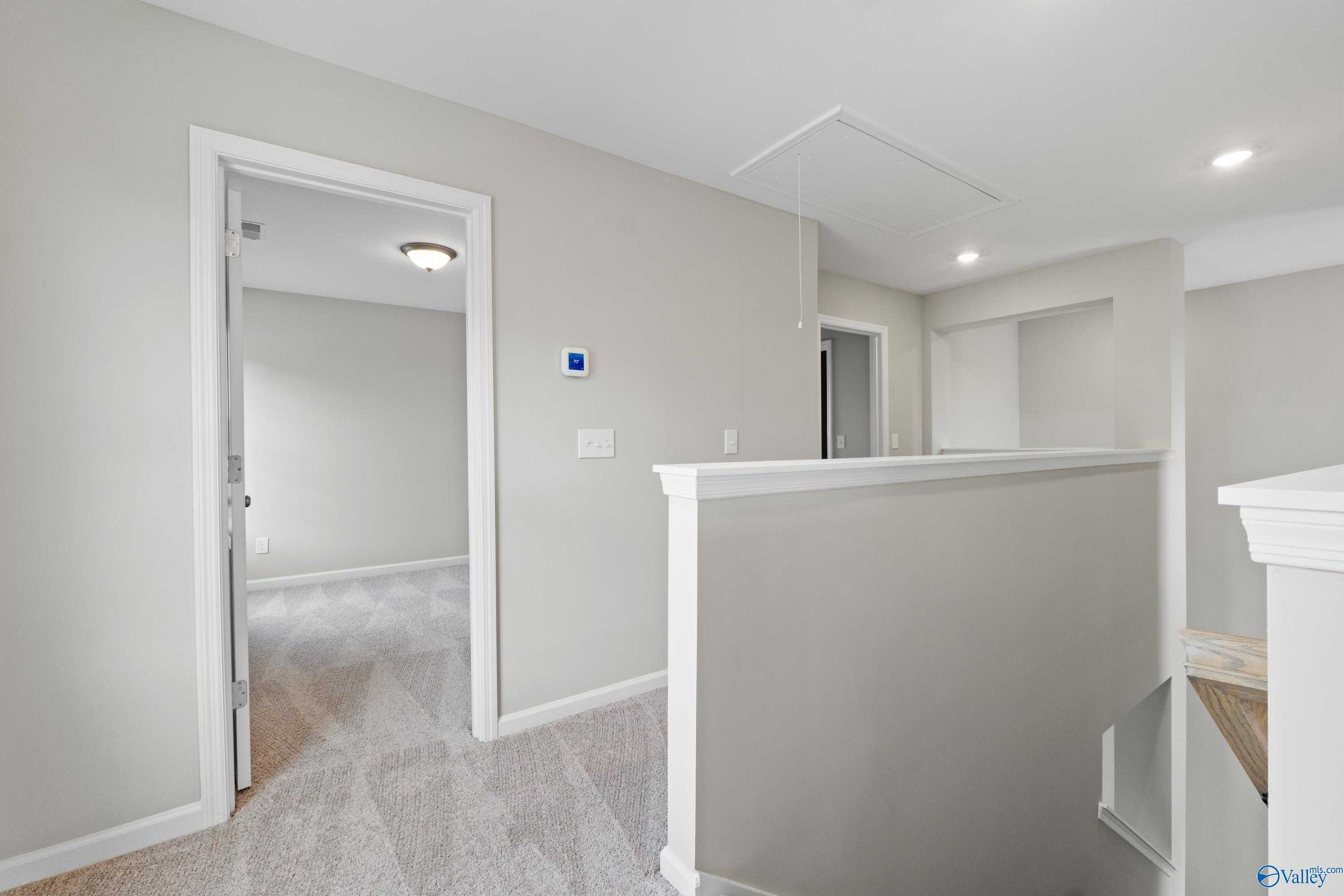 Upper-level hallway with neutral beige walls, carpeted floors, and white railing in Evermore Homes The Augusta, Madison, Alabama