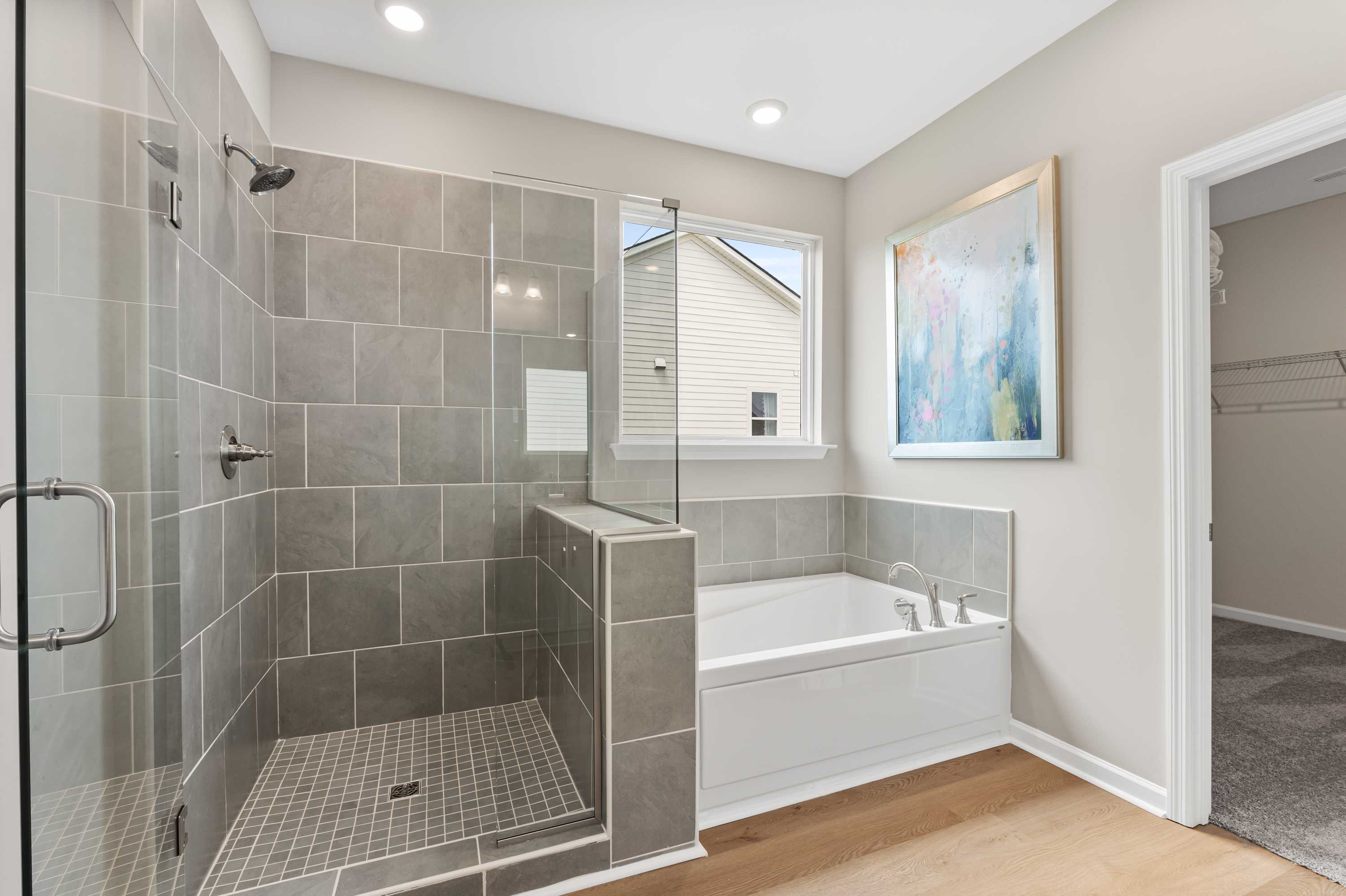 Spacious master bathroom at The Meadows at Hampton Cove in Owens Cross Roads AL featuring gray tiled walk-in shower and freestanding soaking tub
