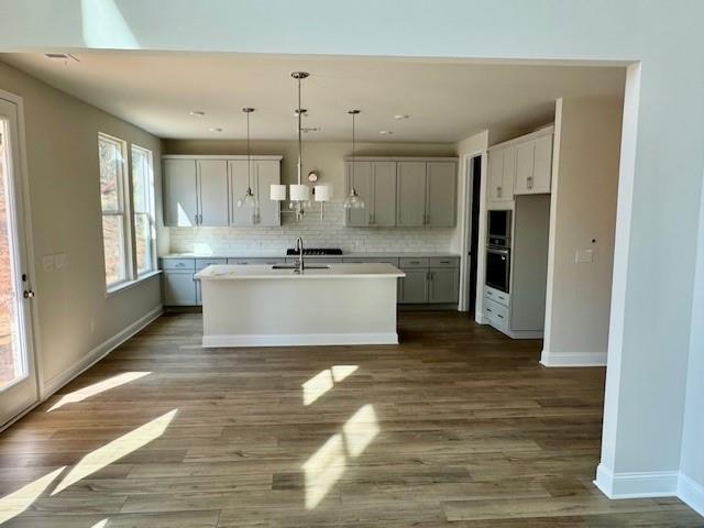 Modern white kitchen with shaker cabinets, large center island, stainless appliances, subway tile backsplash, and hardwood floors in The Danbury C, Buford, GA
