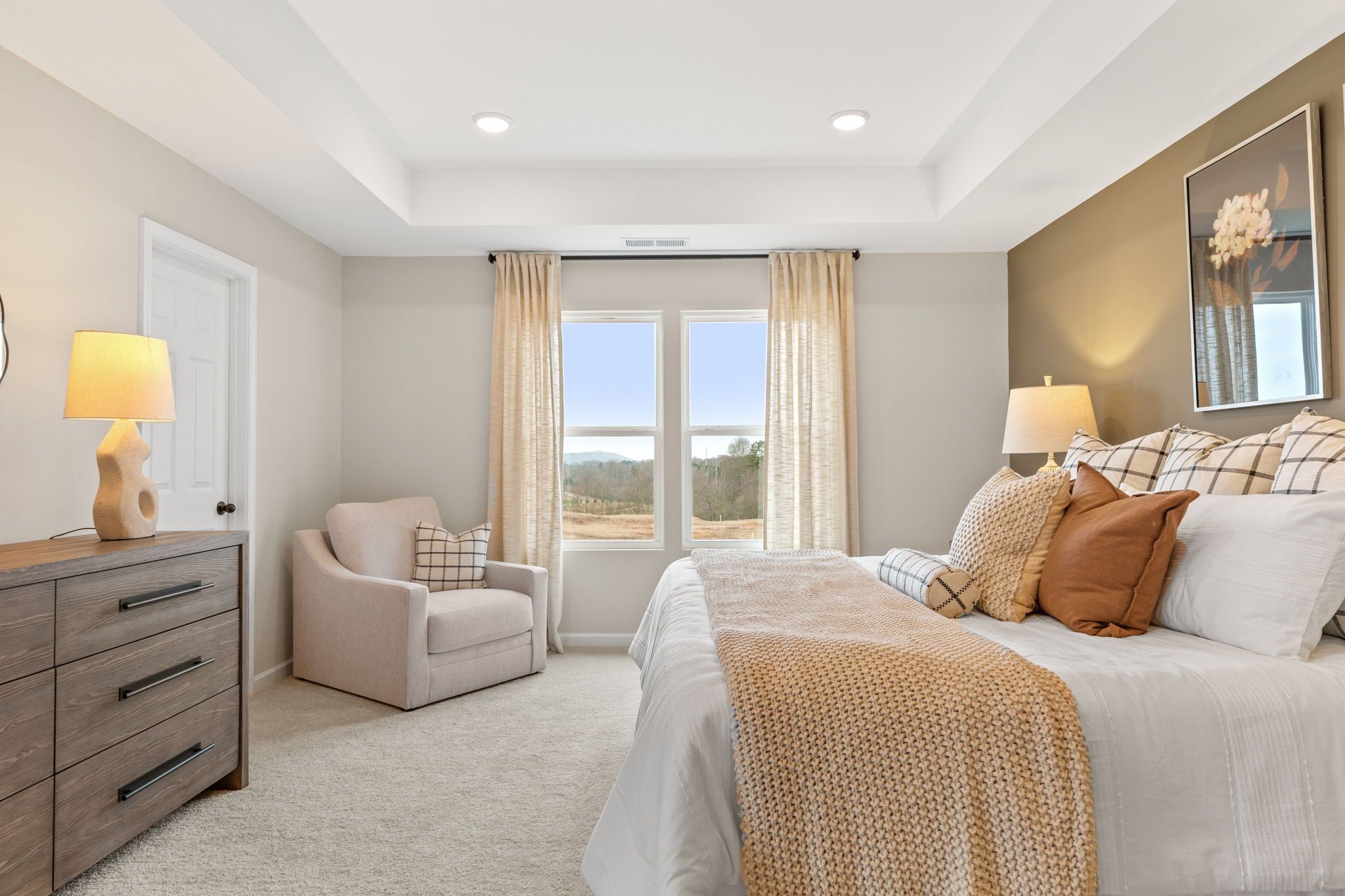 Spacious master bedroom in Hemingway Cumming GA with king bed neutral tones large windows scenic view and wooden dresser