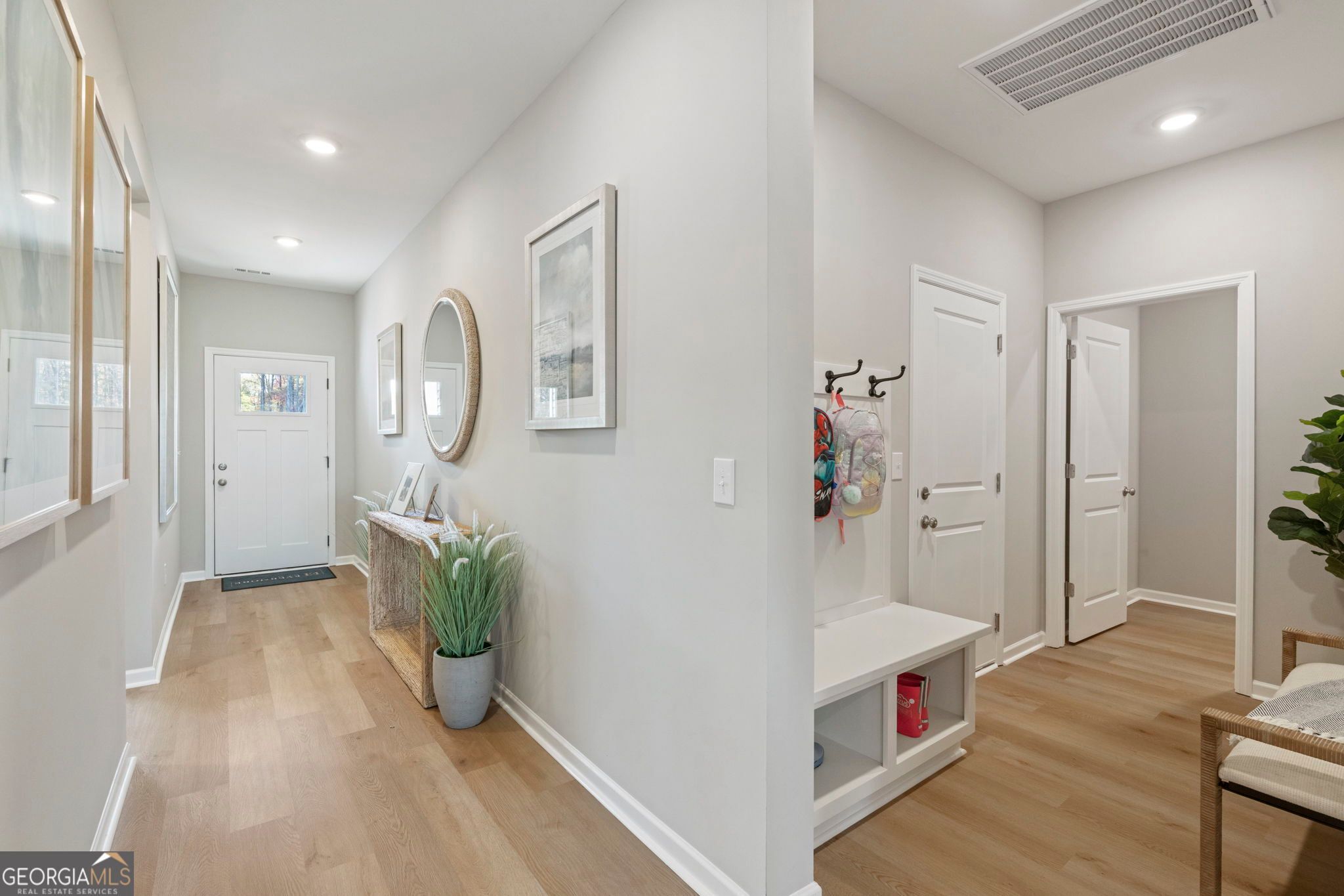 Bright entry foyer with white walls, oak hardwood floors, console table with plants, coat hooks and bench in Evermore Homes The Phoenix, Perry, Georgia