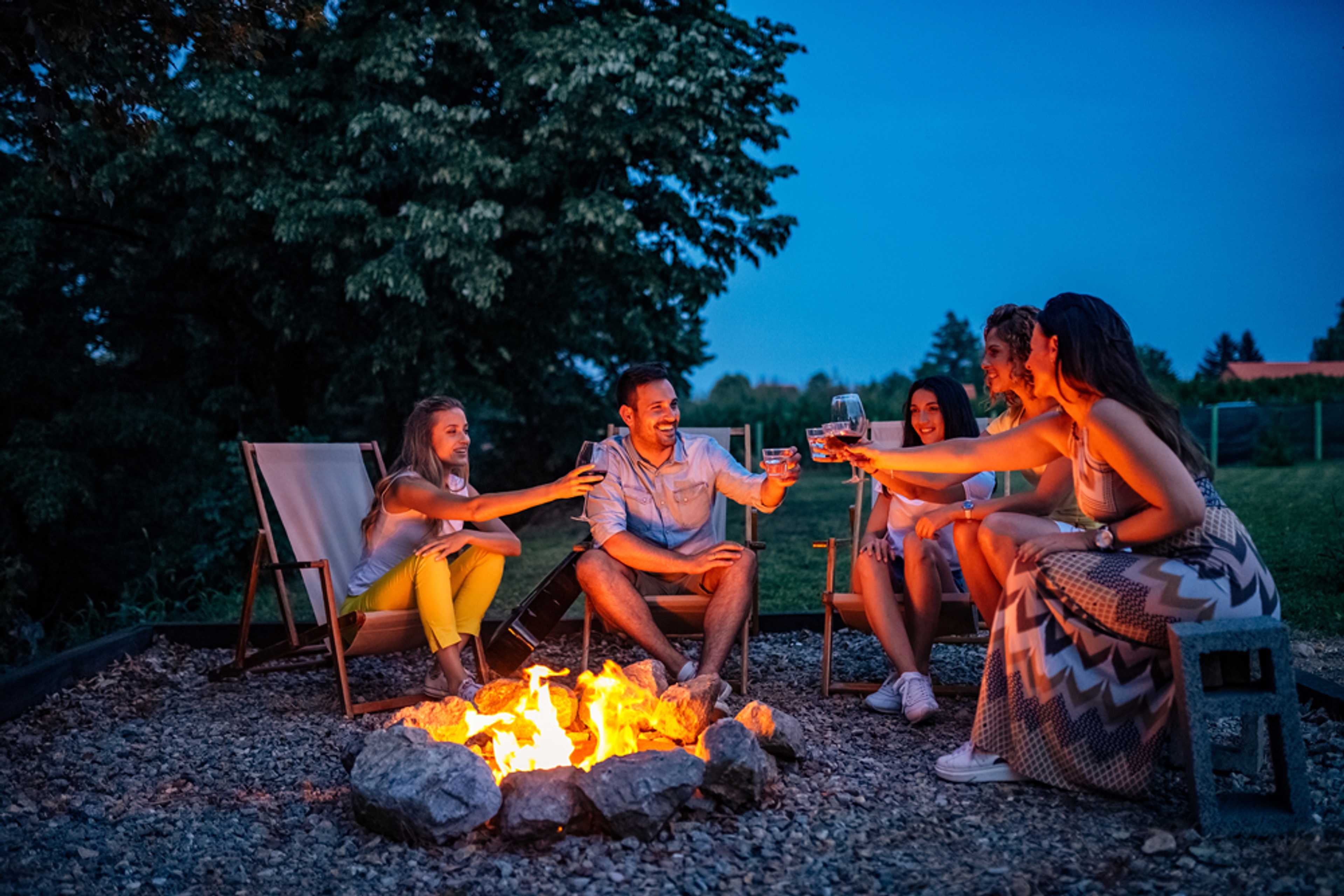 Family toasting drinks around stone fire pit at dusk in Emberly community, Beasley Texas by Davidson Homes