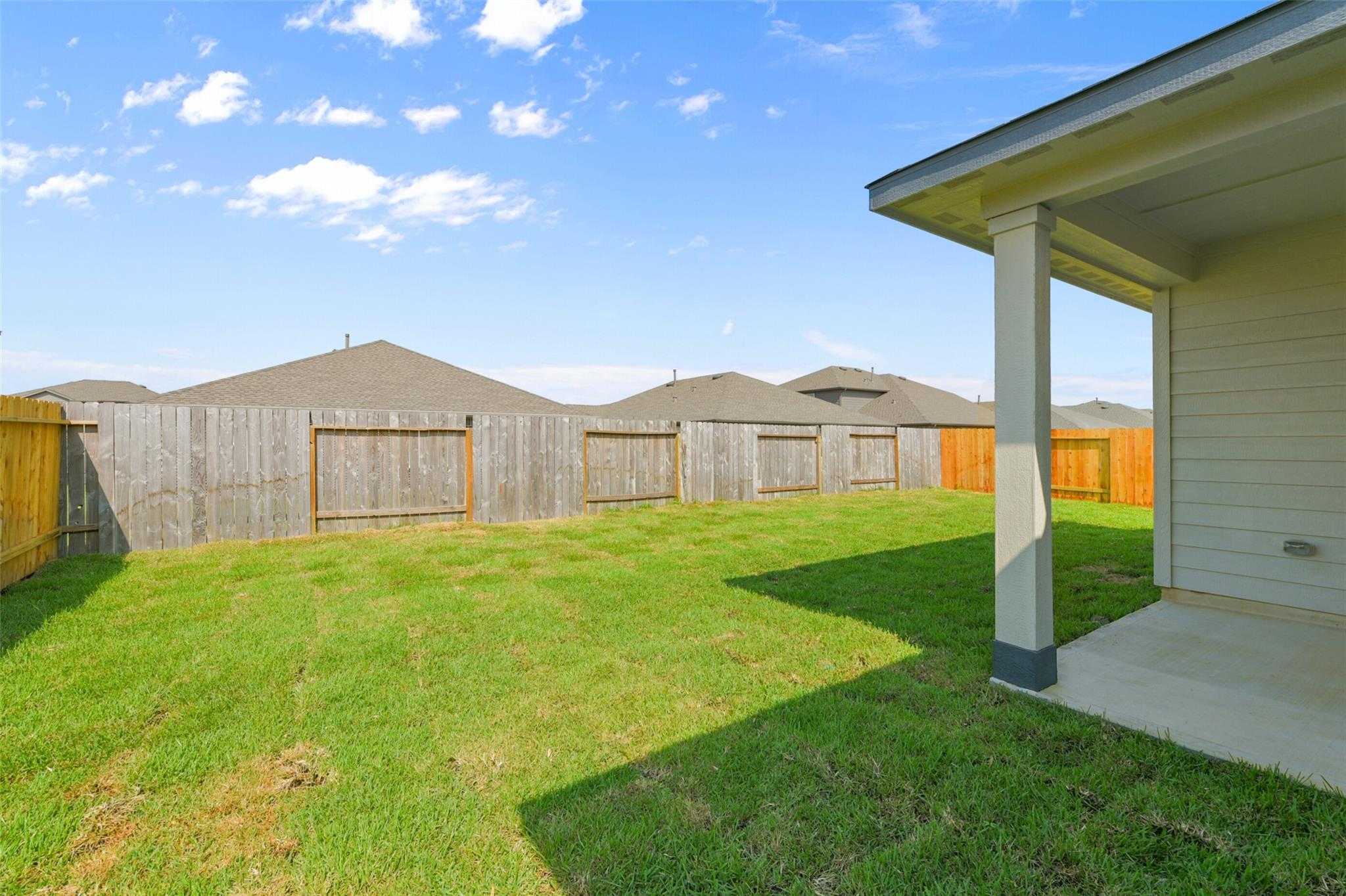 Private backyard with lush green lawn, covered patio, and wooden privacy fences in Davidson Homes The Laguna B, Dayton, Texas