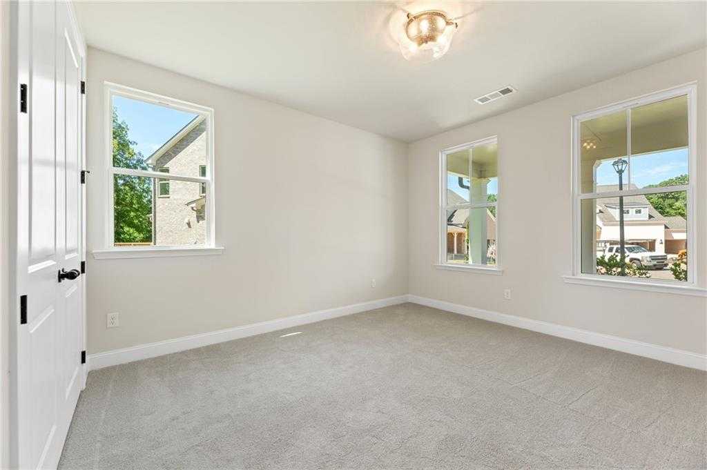 Bright bedroom with beige walls, carpet flooring, large windows, and chandelier in Davidson Homes The Hickory E, Buford