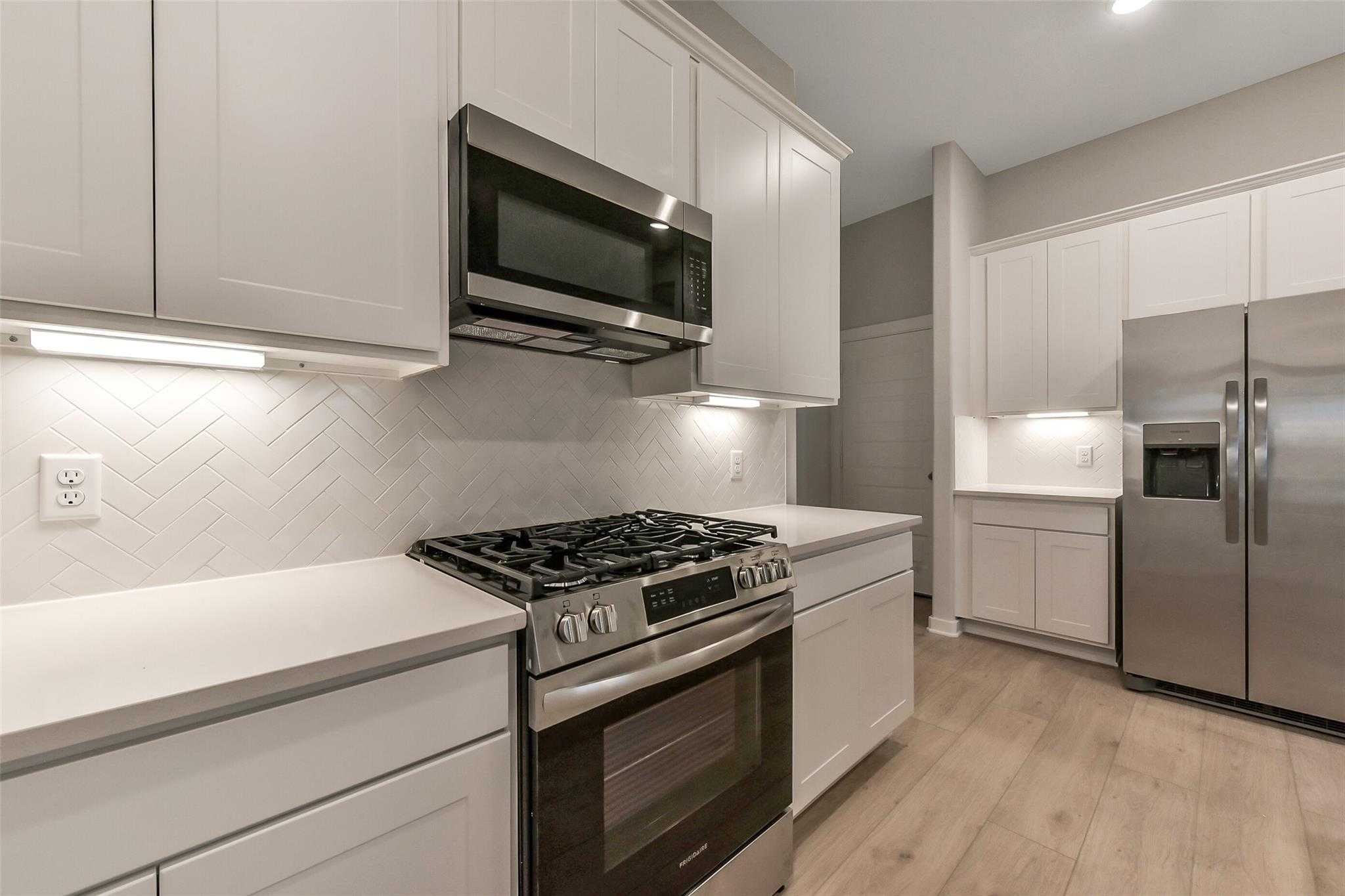 Modern white kitchen with stainless steel appliances, subway tile backsplash, quartz counters in Davidson Homes The Laguna B, Katy, Texas