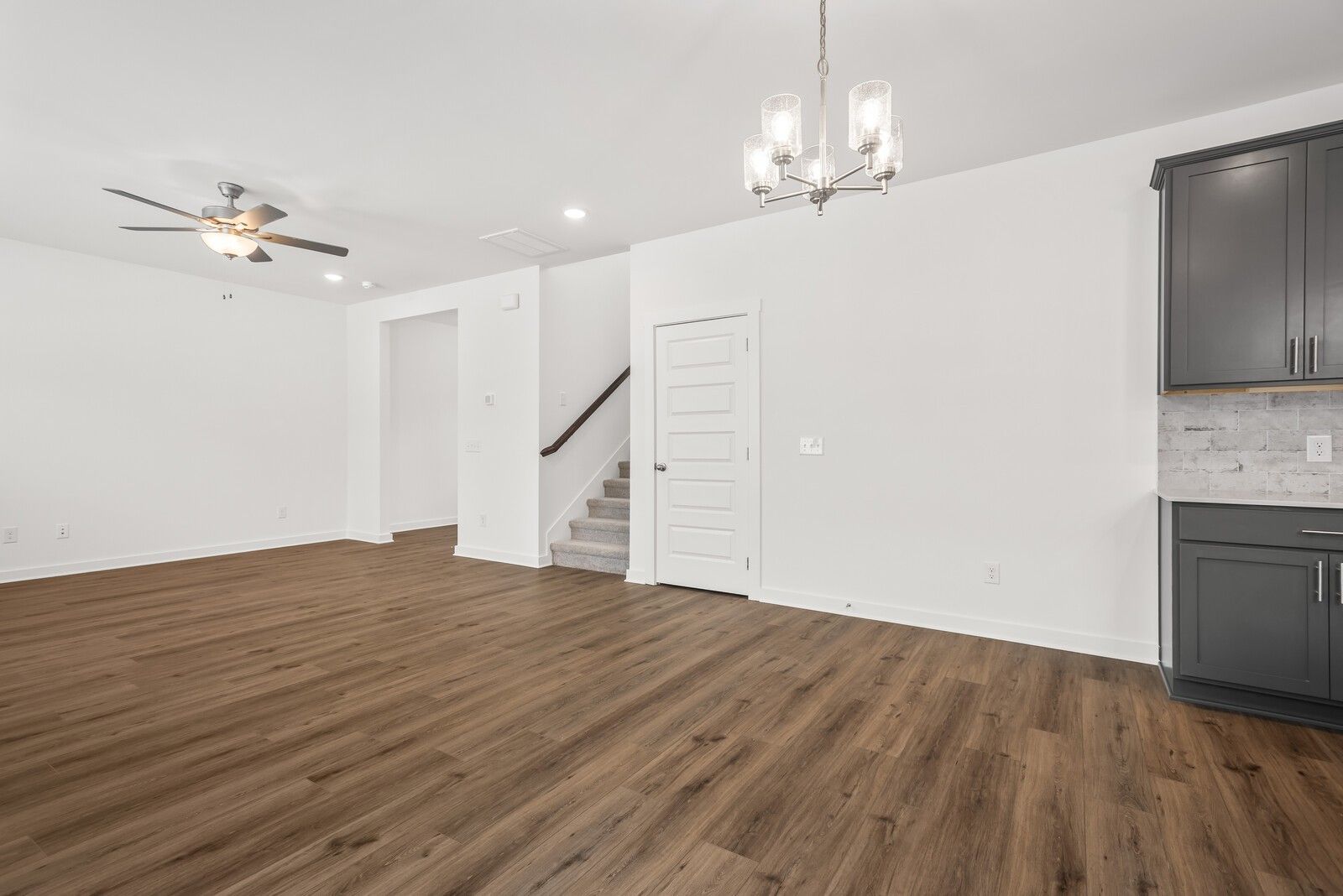 Open entry foyer with hardwood floors, ceiling fan, chandelier, staircase, and dark cabinet kitchen in Davidson Homes The Gordon C, White House, TN