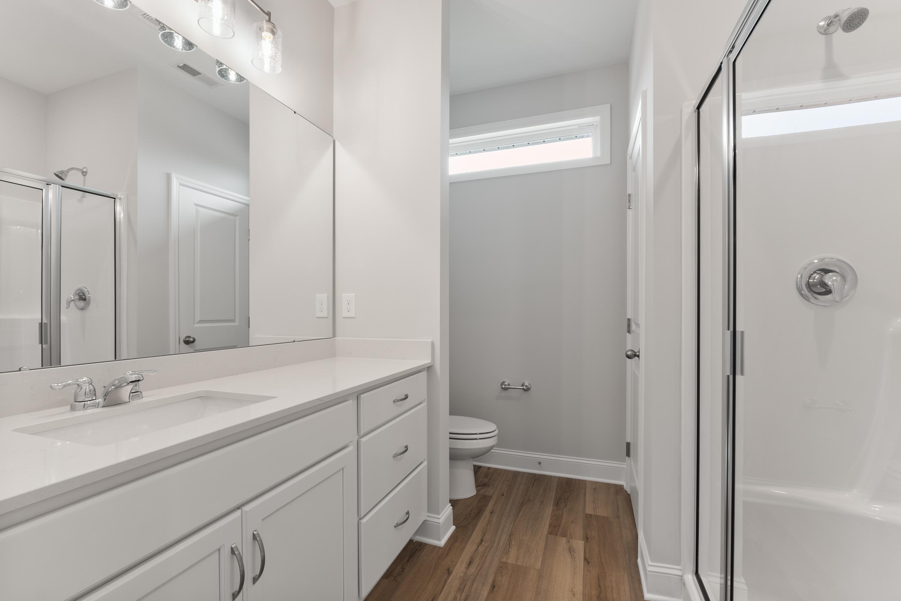 Spacious master bathroom in The Butler by Davidson Homes featuring white vanity, large mirror, glass walk-in shower, and light wood floors