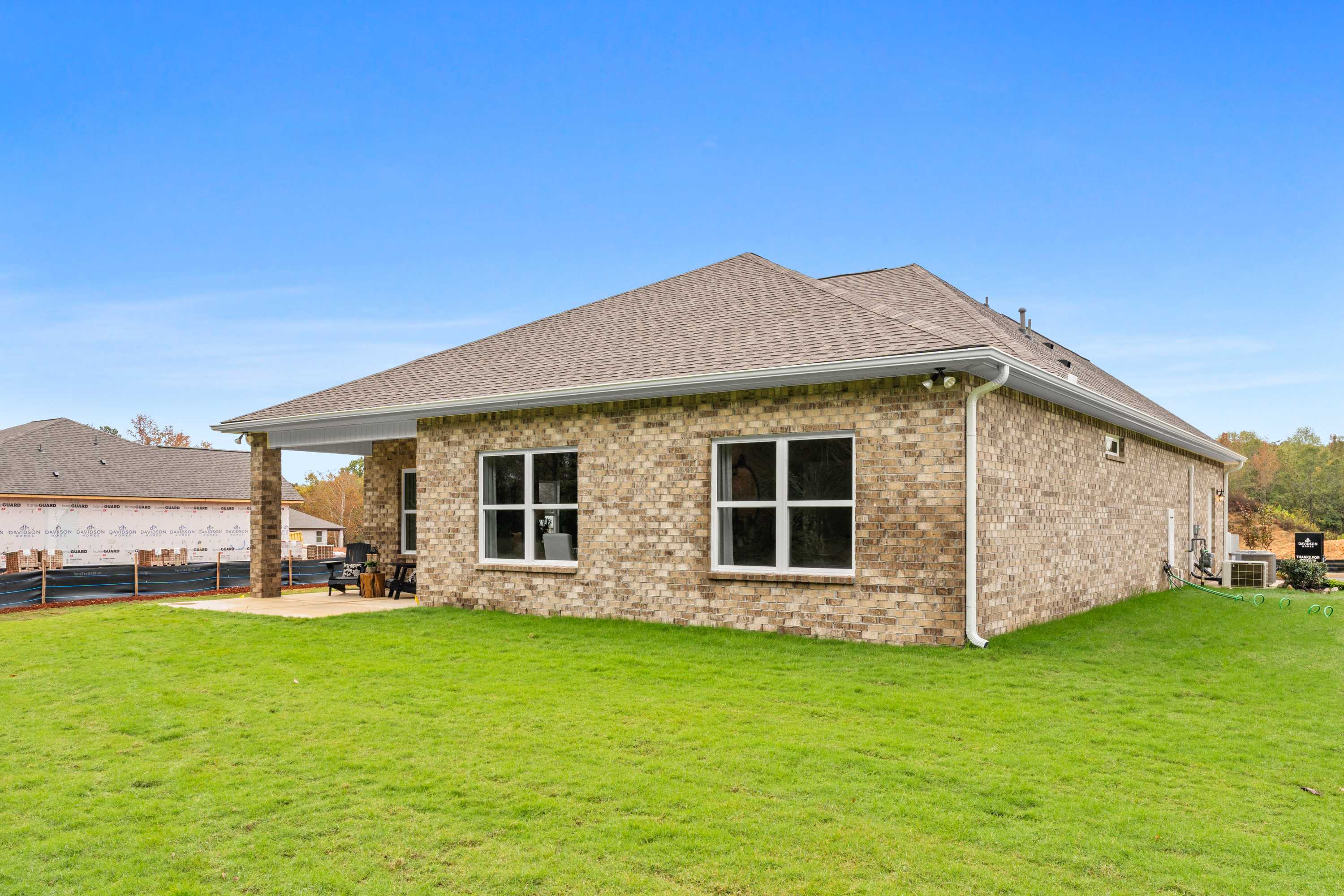 Brick home side exterior at Spragins Cove in Huntsville Alabama with covered porch, large windows, and lush green lawn