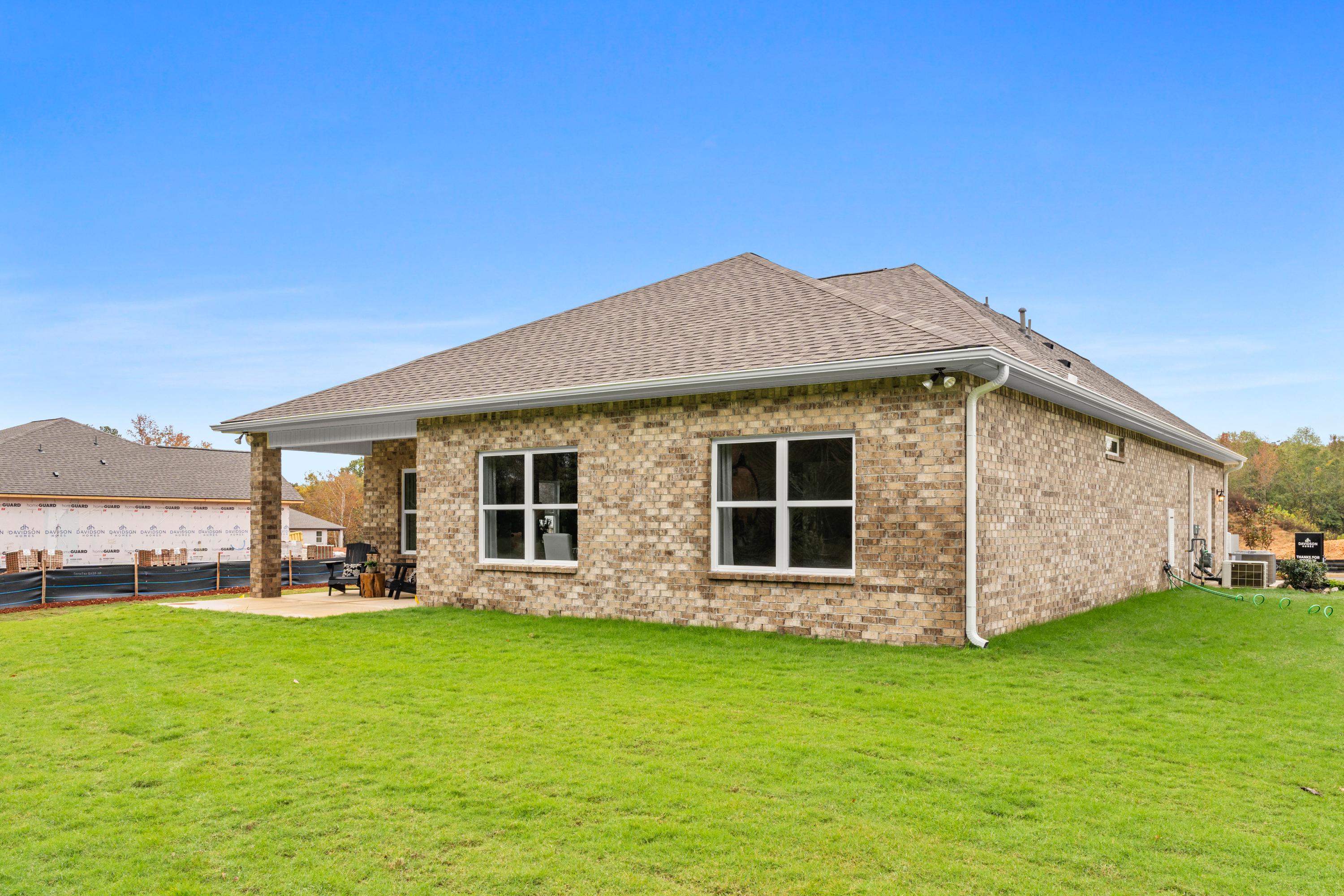 Brick home side exterior at Spragins Cove in Huntsville Alabama with covered porch, large windows, and lush green lawn