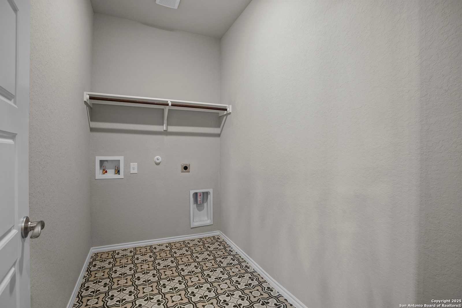 Functional laundry room with built-in shelves, washer/dryer hookups, pet door, and patterned tile floor in Davidson Homes The Collin B, Seguin, Texas