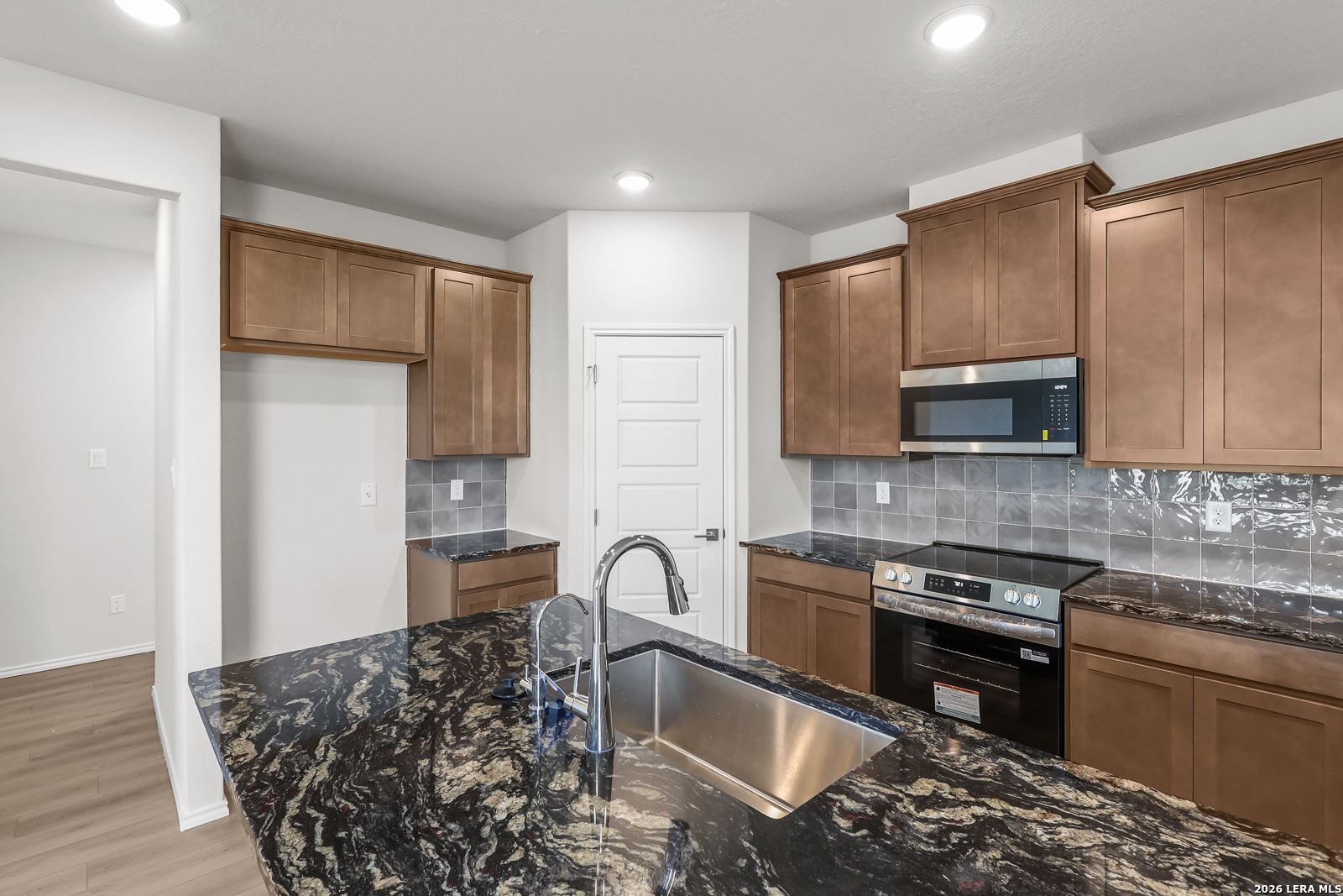 Modern kitchen with granite island, stainless steel appliances, and wood cabinetry in The San Marcos F, San Antonio home.