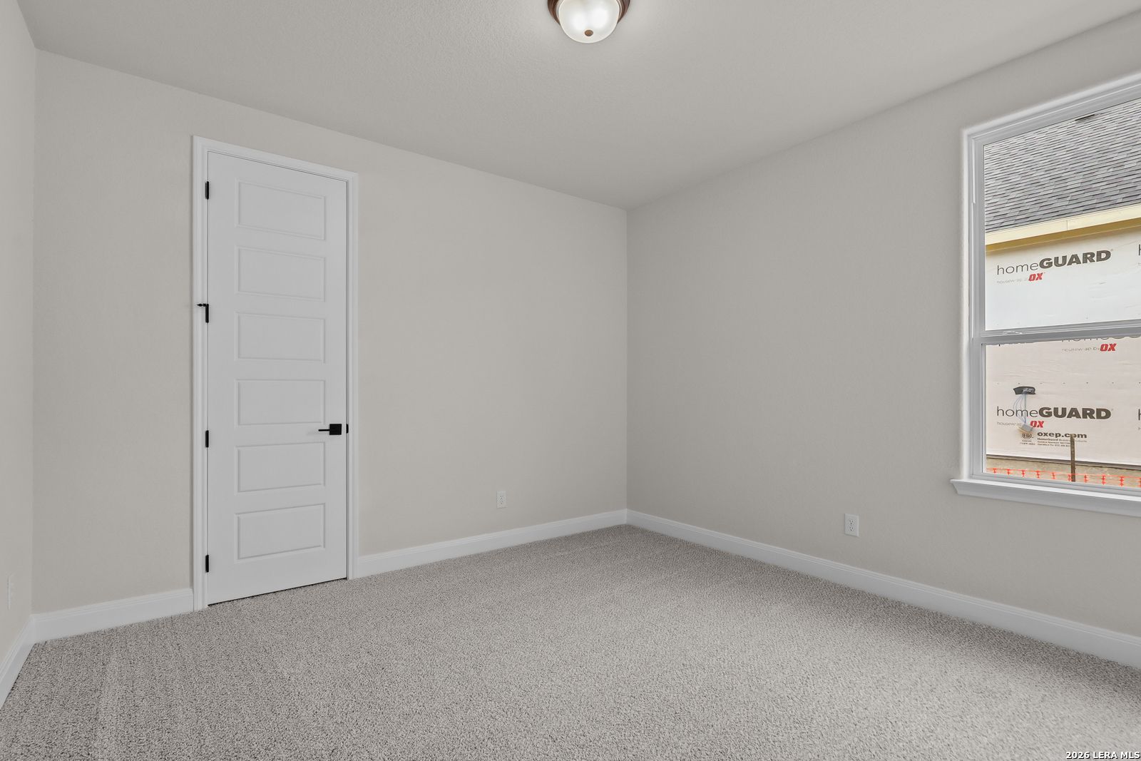 Spacious empty bedroom with beige walls, gray carpet, and large window in Davidson Homes The Lanier G, Castroville, Texas