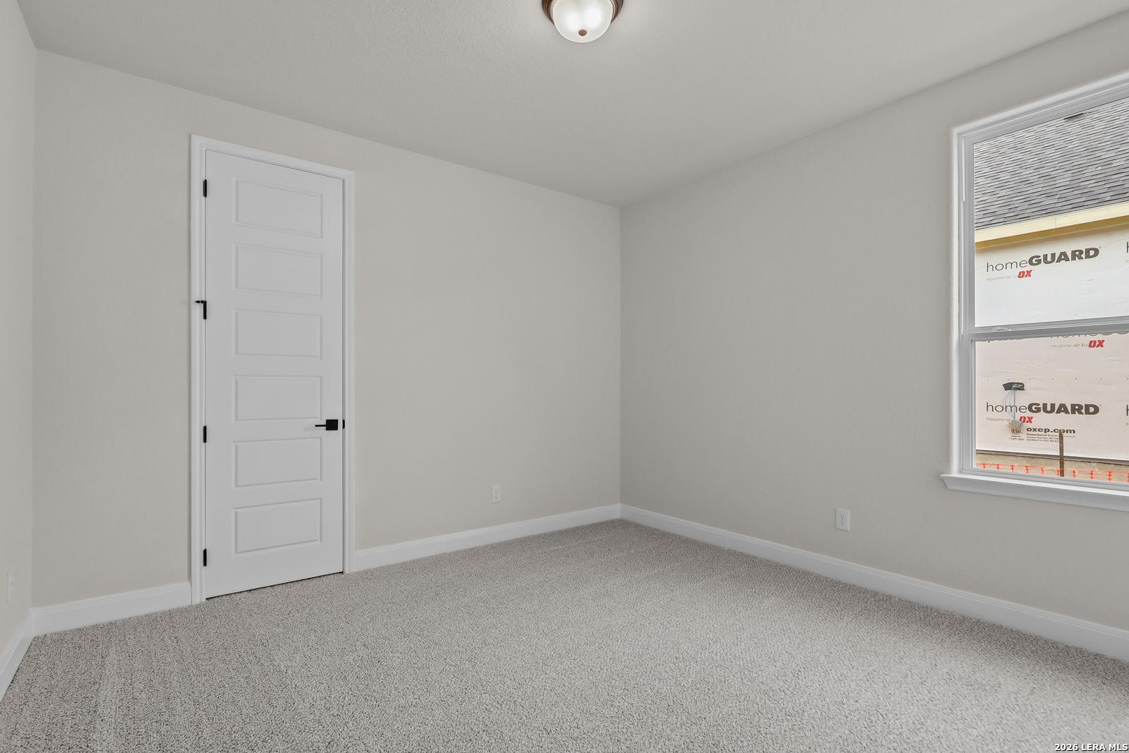 Spacious empty bedroom with beige walls, gray carpet, and large window in Davidson Homes The Lanier G, Castroville, Texas