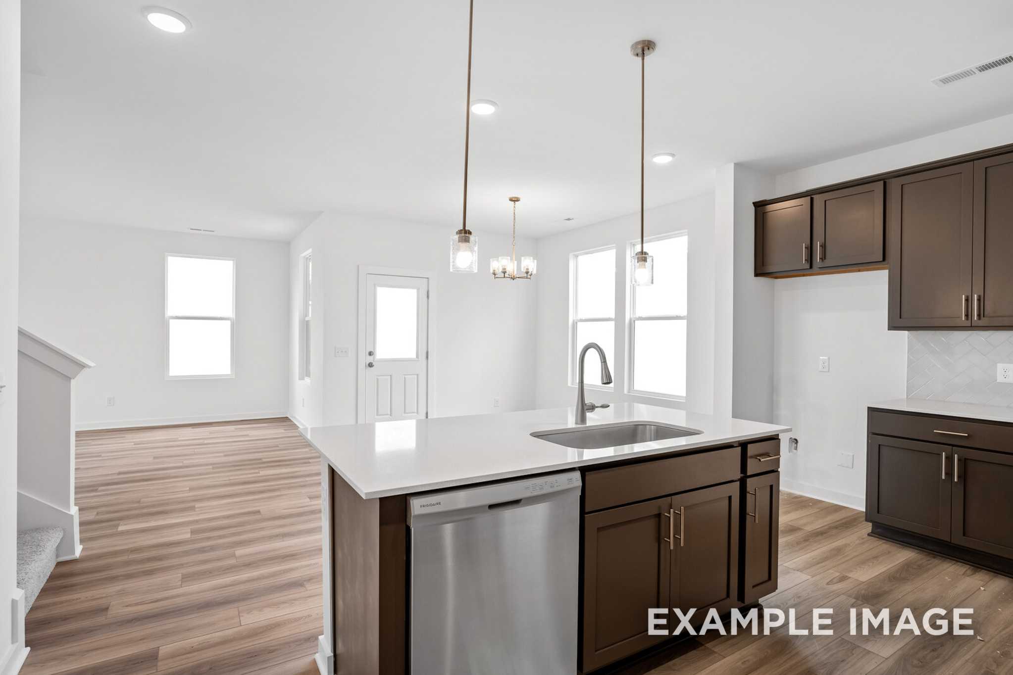 Spacious modern kitchen in The Murray B with dark wood cabinets, white quartz island, farmhouse sink, and open living area